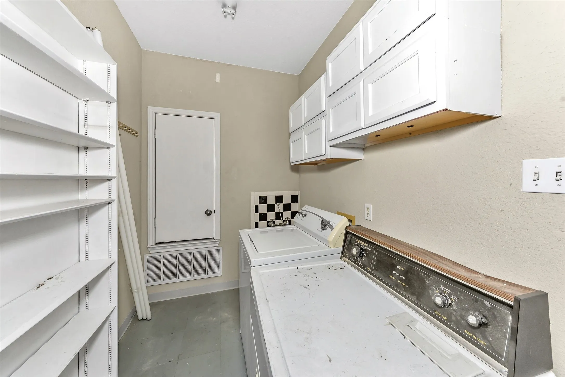 Utility room featuring ample built-in shelving, white overhead cabinetry, and light-toned walls