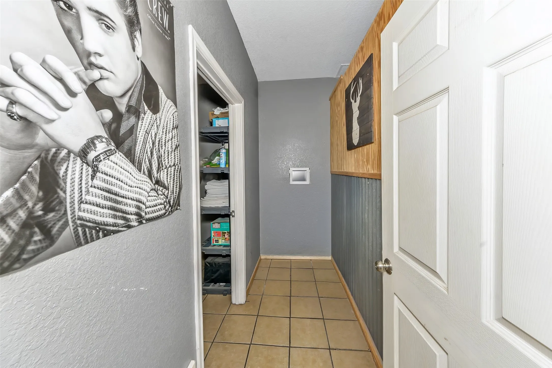 Hallway with tiled flooring, a built-in storage closet, a white paneled door, and a wall featuring a wood-panel and corrugated metal wainscoting