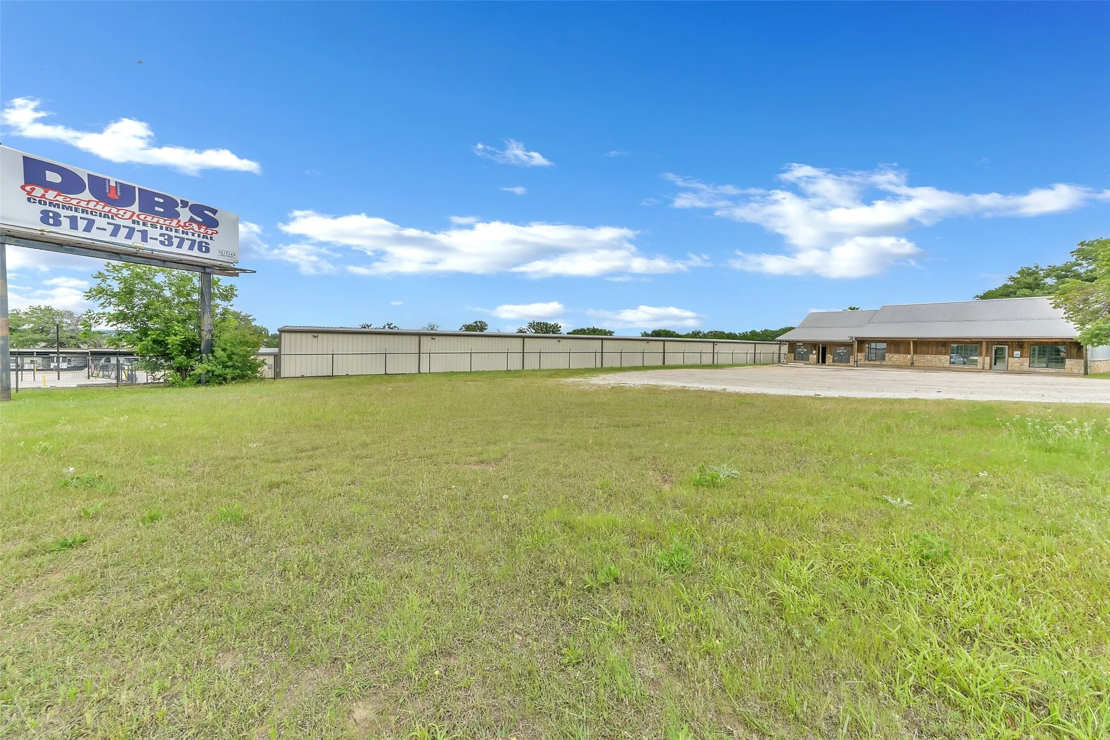 Expansive grassy lot featuring a commercial building with stone accents, a metal roof, and an asphalt parking area