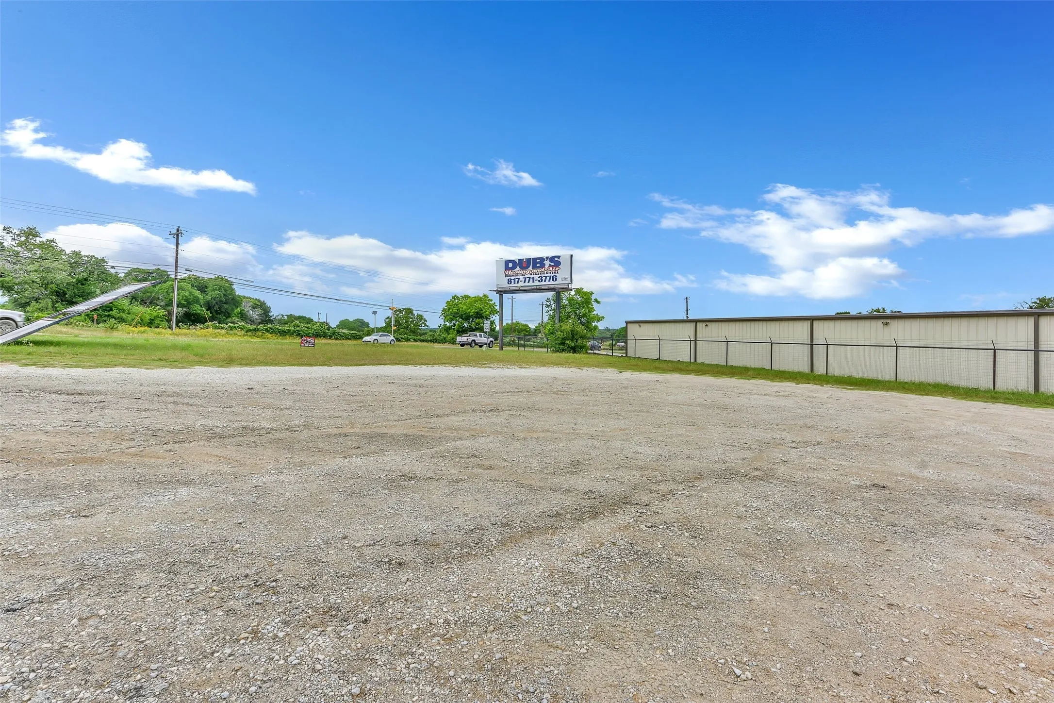 Expansive gravel parking area with a metal chain-link fence bordering a large commercial building