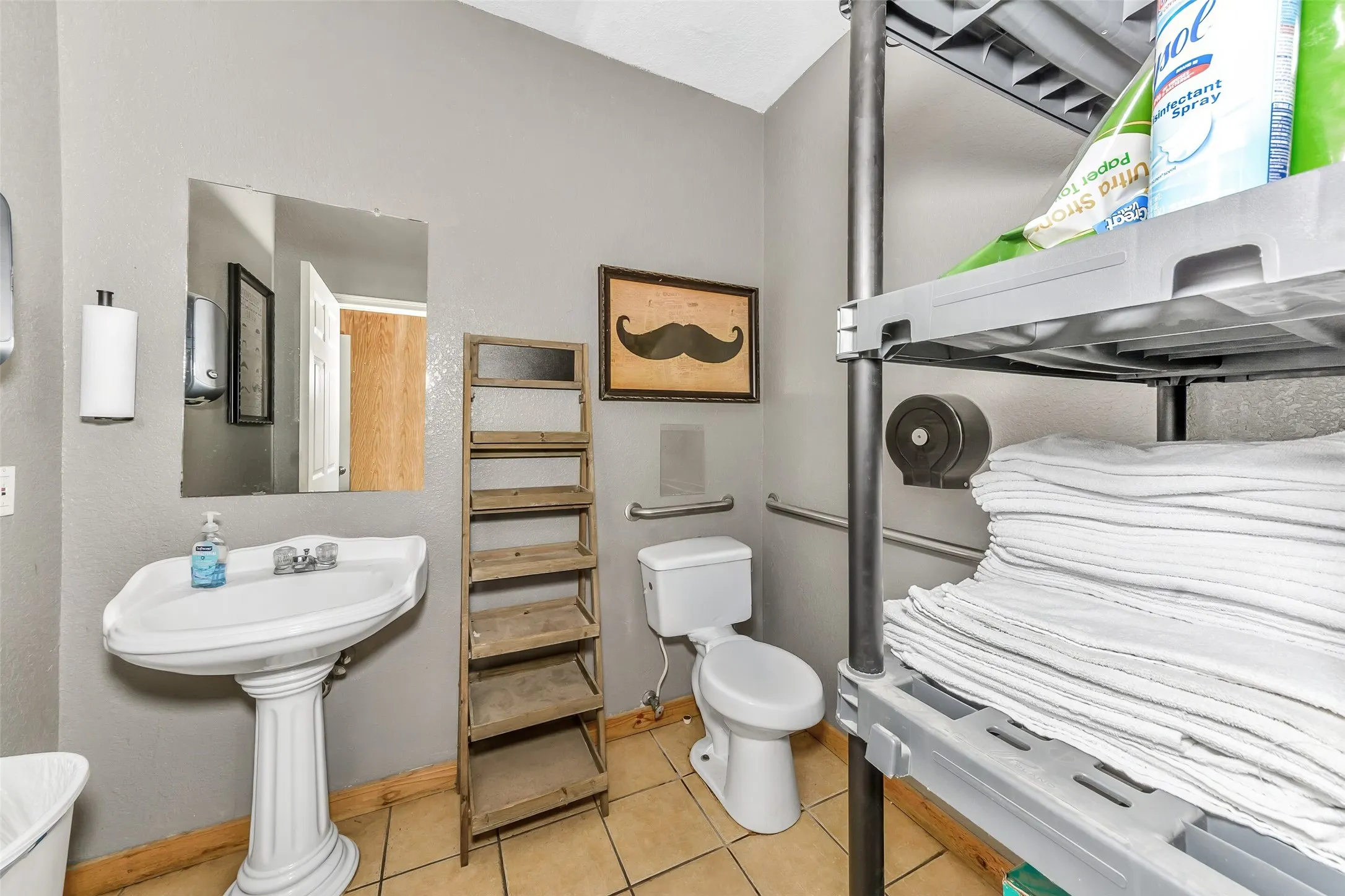 Restroom featuring a pedestal sink, white toilet, grab bars, and tile flooring
