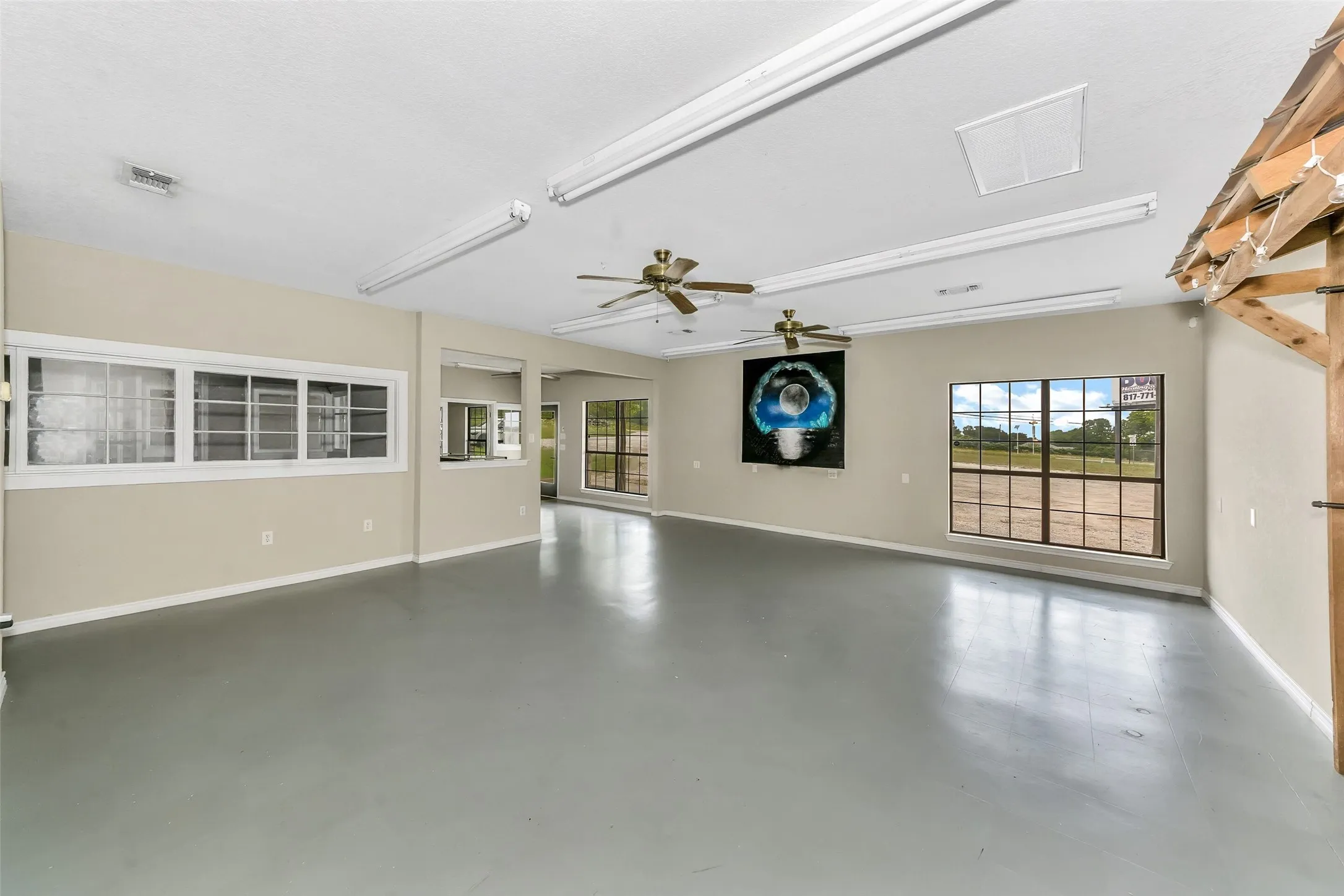 Spacious open-concept room featuring high ceilings, durable gray flooring, and multiple large windows for abundant natural light