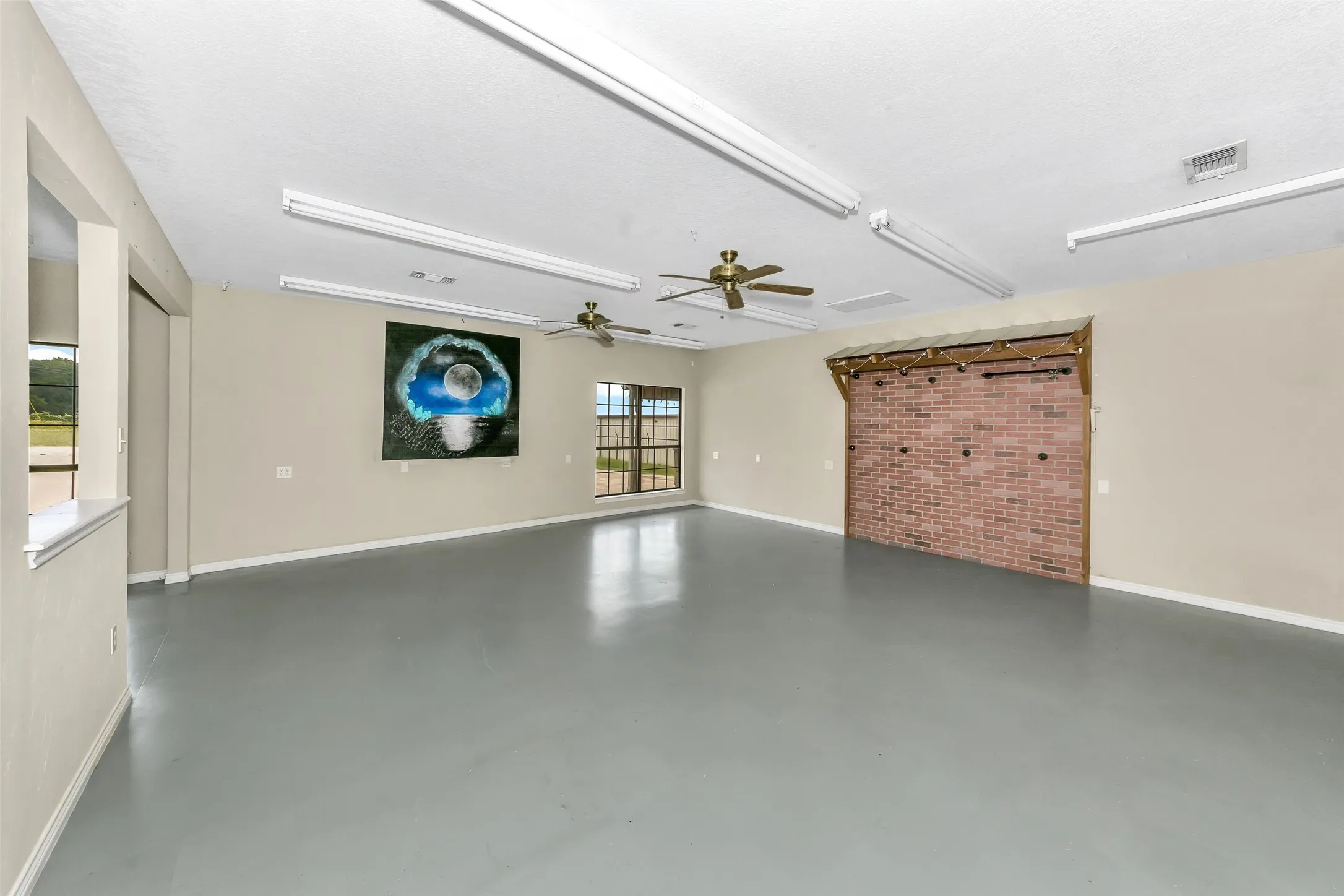 Spacious open-concept room featuring light gray flooring, neutral wall paint, and multiple ceiling-mounted fluorescent light fixtures