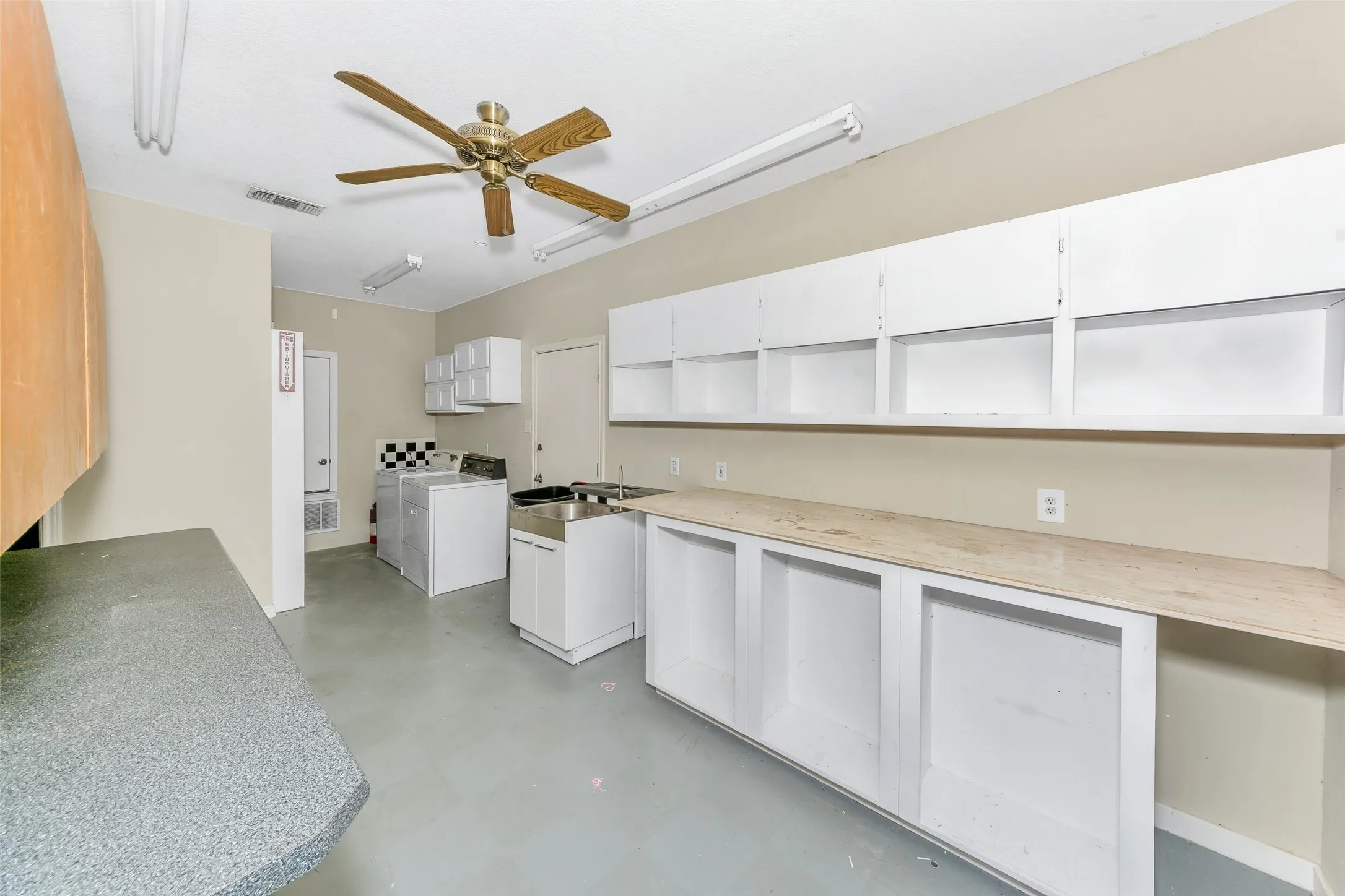 Utility room featuring extensive built-in cabinetry, durable flooring, a stainless steel utility sink, and a ceiling fan with integrated lighting