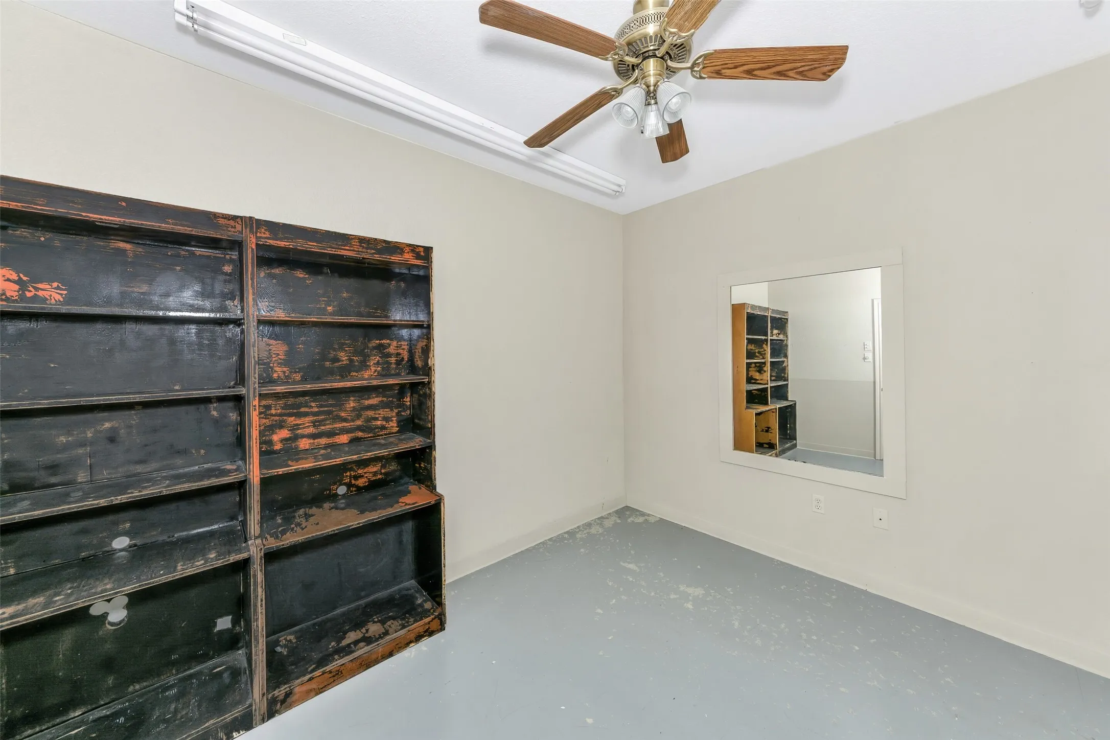 Interior space featuring a ceiling fan with wood-finish blades, fluorescent strip lighting, and a wall-mounted mirror