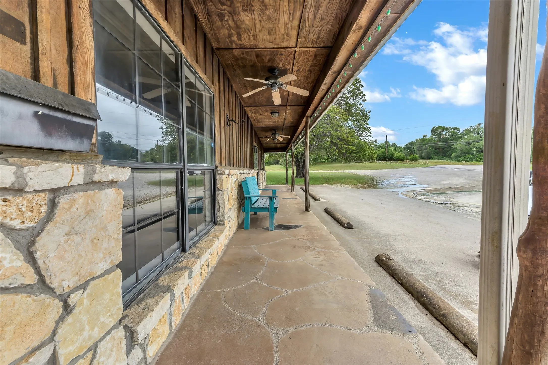 Expansive covered porch featuring a flagstone-style concrete surface, stone base, large paned windows, wood-paneled walls, and built-in ceiling fans