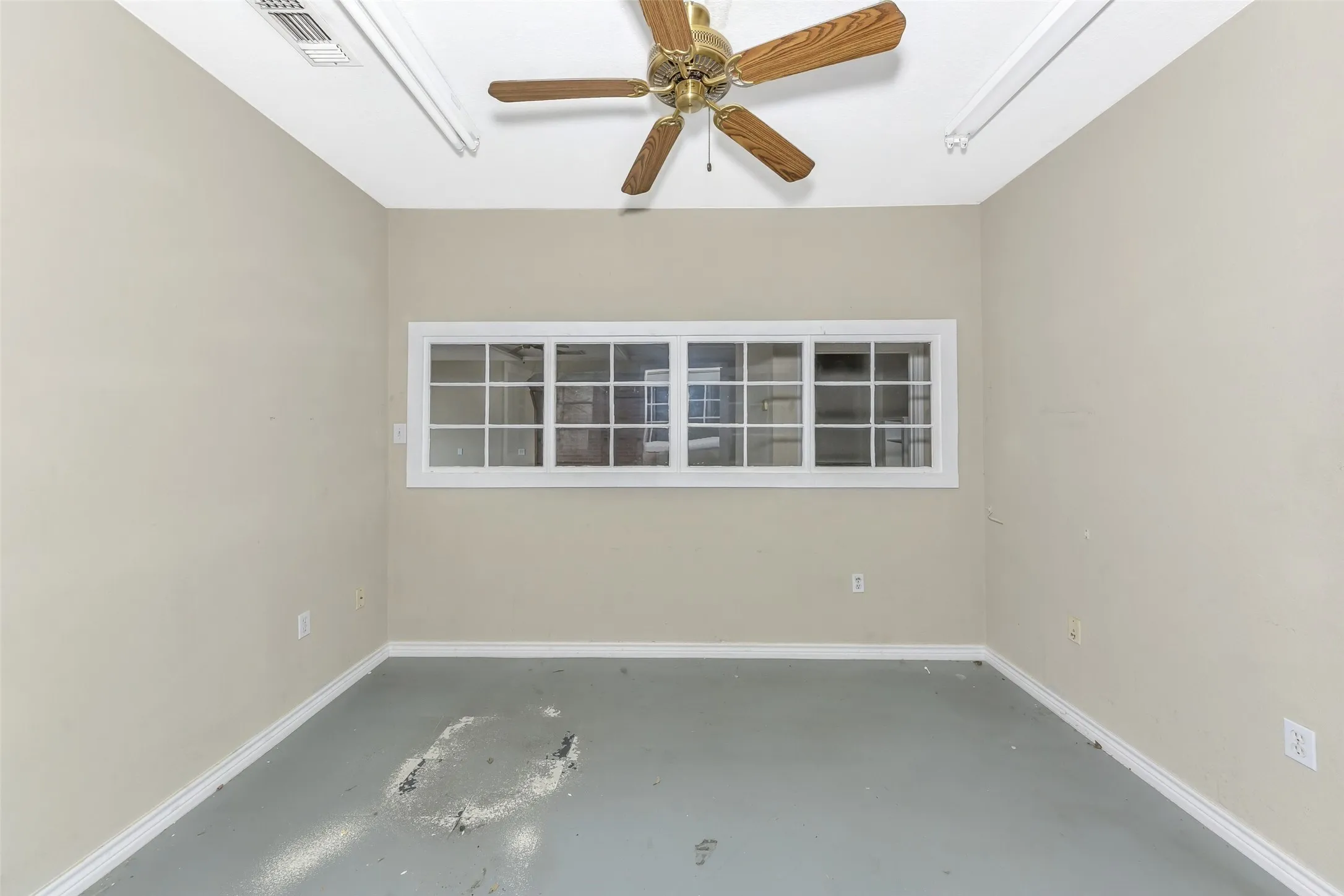 Interior room featuring a horizontal window with white trim, a ceiling fan with wood-finish blades, and painted walls