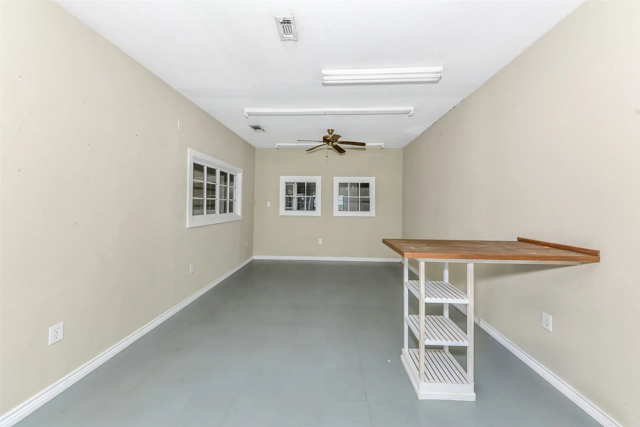 Spacious room featuring multiple windows, a ceiling fan, and fluorescent lighting