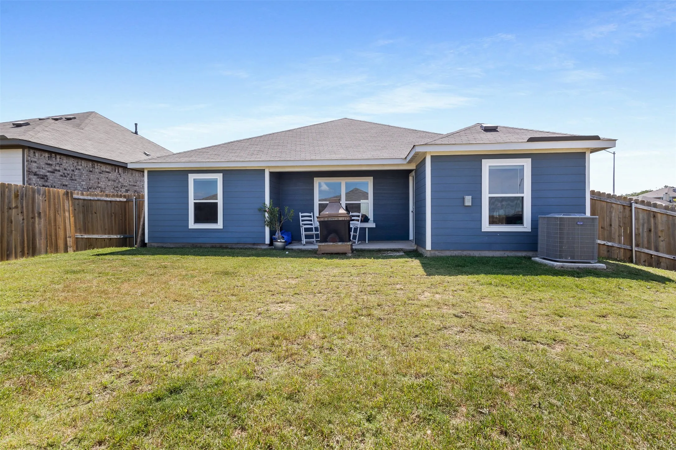 Expansive rear yard featuring a concrete patio, blue siding, white trim windows, and a complete wood fence surround