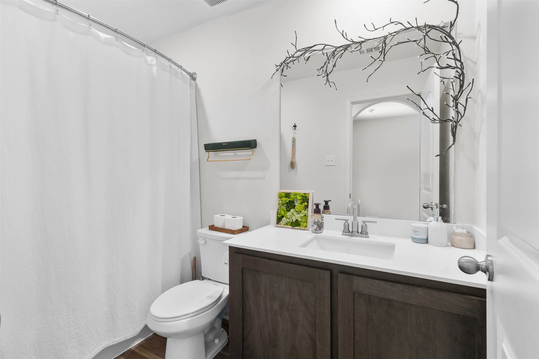 Bathroom featuring a dark wood-finish vanity with a white countertop and integrated sink, a large wall-mounted mirror, and wood-finish flooring