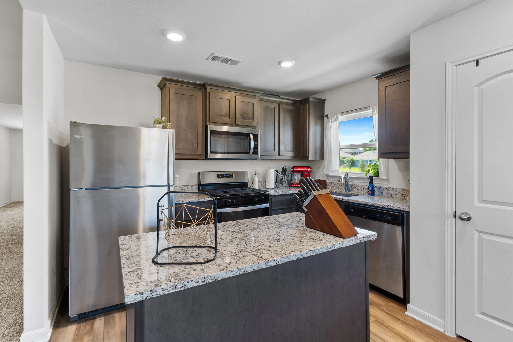 Modern kitchen featuring wood-finish flooring, recessed lighting, and stainless steel appliances including a refrigerator, range, microwave, and dishwasher