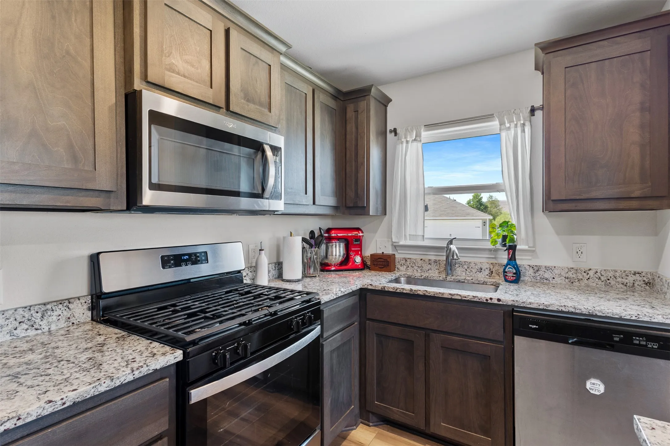 Modern kitchen featuring wood cabinetry, stainless steel appliances, granite-style countertops, and a window above the sink