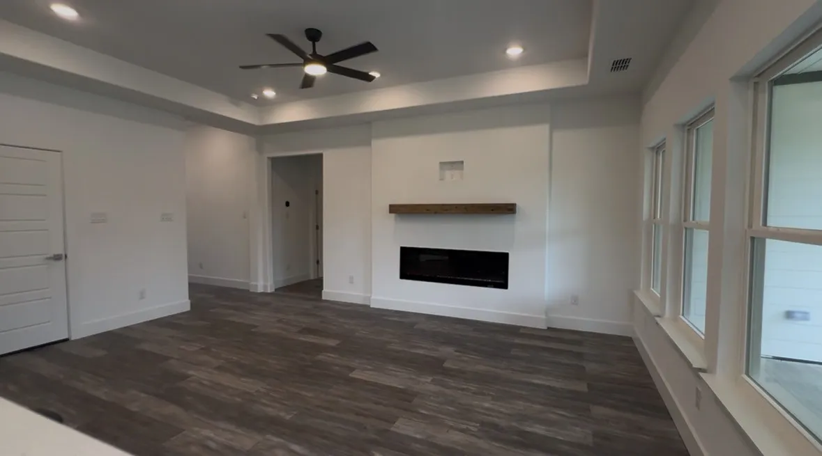 Spacious living area featuring a modern linear fireplace with a wood mantel, wood-finish flooring, recessed lighting, a ceiling fan, and multiple windows