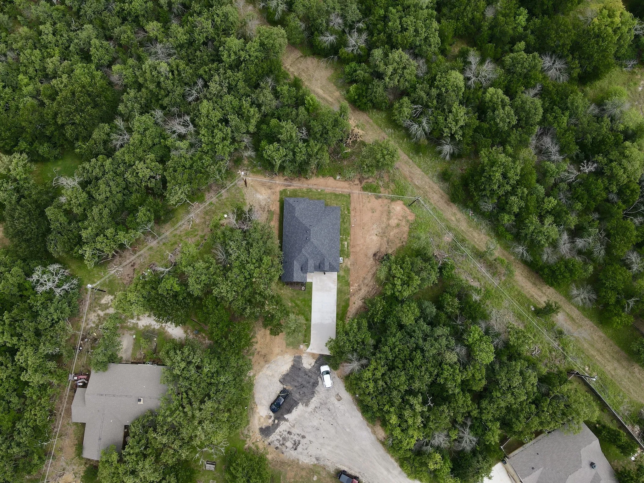 New construction home with a dark shingled roof, concrete driveway, and surrounding green tree canopy