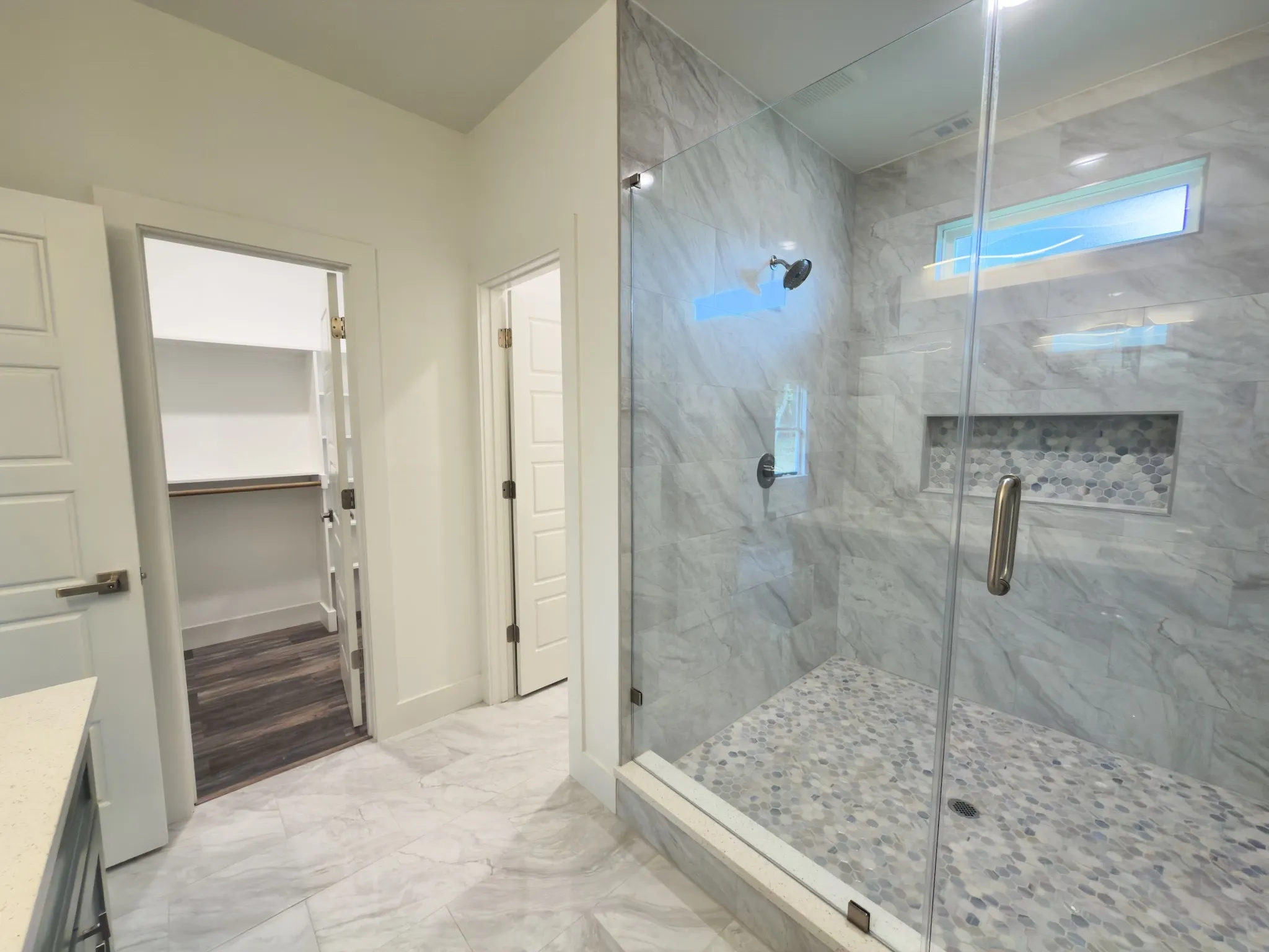 Spacious walk-in shower featuring a glass enclosure, gray-veined tile walls, and a mosaic tile shower floor