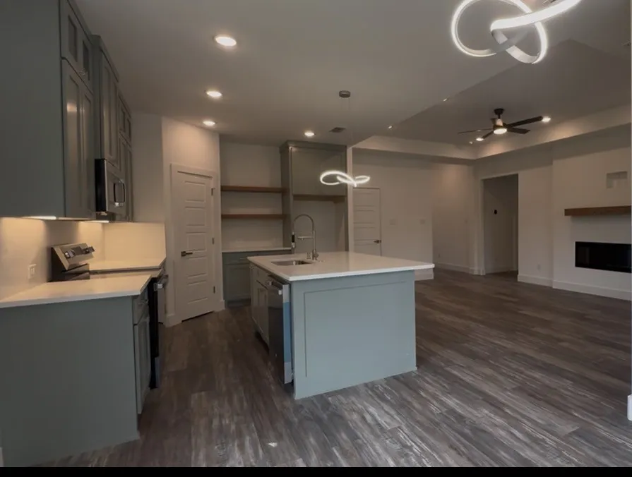 Open-concept kitchen featuring sage cabinetry, a central island with sink, white countertops, stainless steel appliances, and recessed lighting