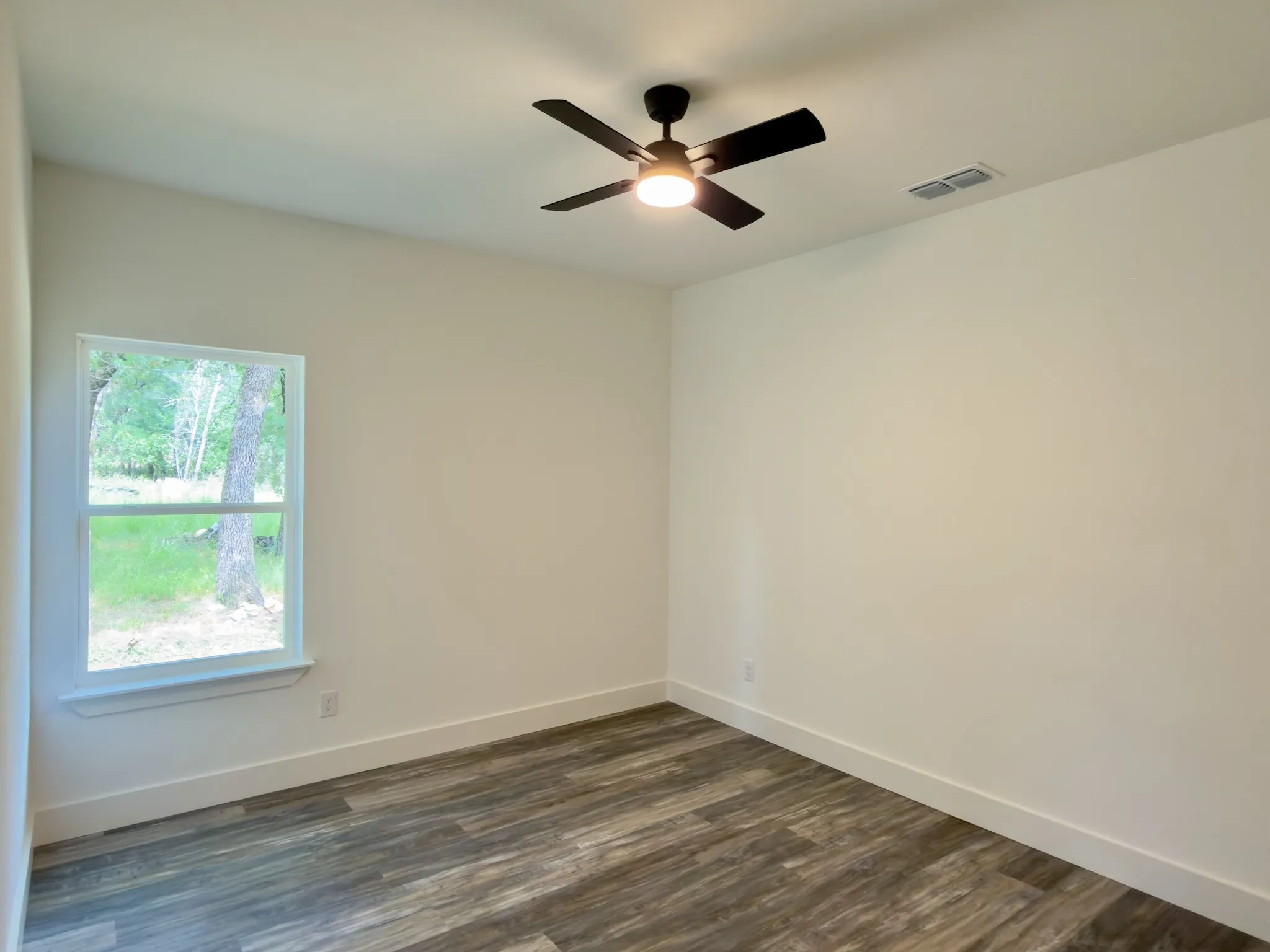 Room featuring wood-finish flooring, a contemporary ceiling fan with integrated lighting, and a white-trimmed window