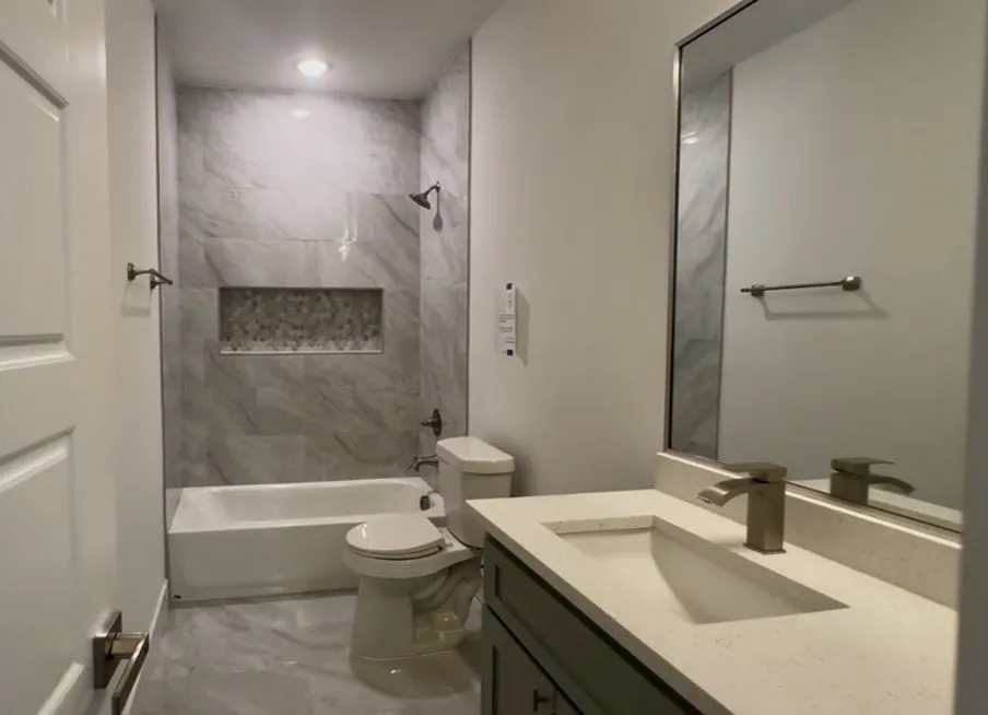 Full bathroom with a tub/shower combination, featuring large format tile surrounds and a decorative mosaic niche