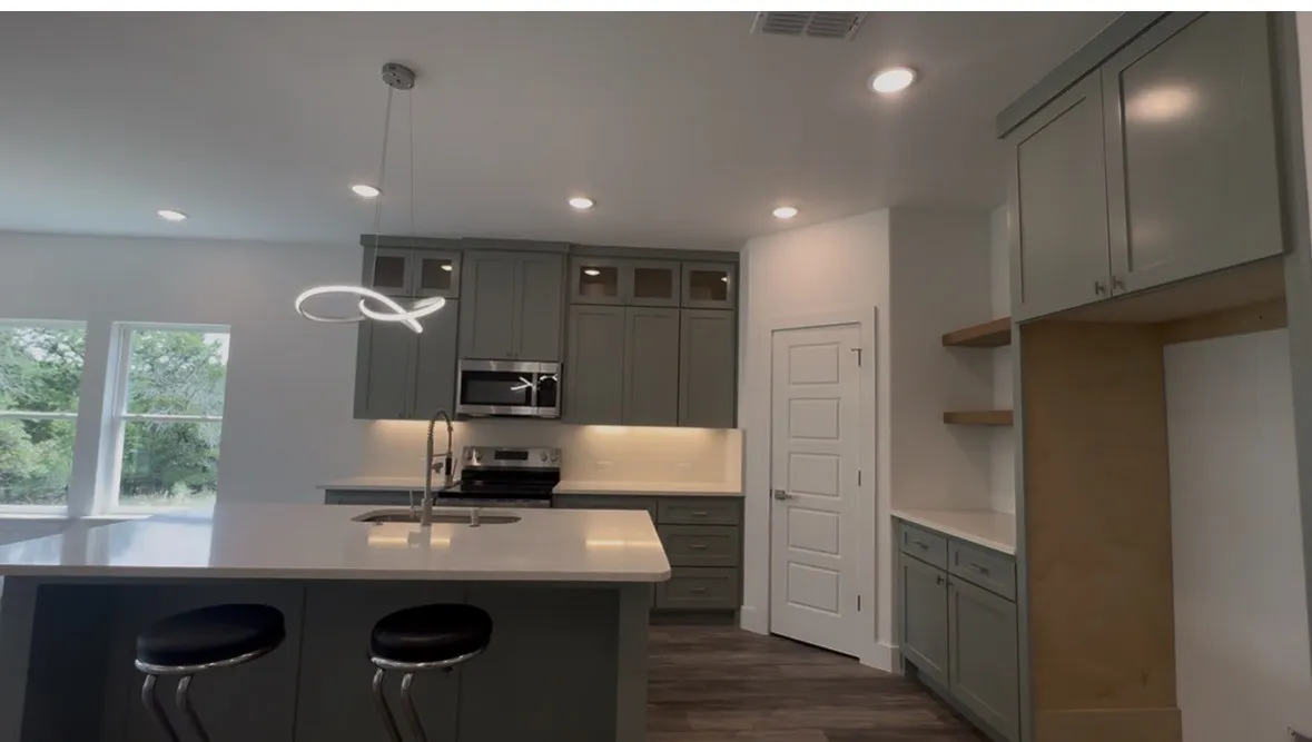Open-concept kitchen featuring an island with an undermount sink, pendant lighting, stainless steel appliances, and abundant cabinetry with under-cabinet lighting