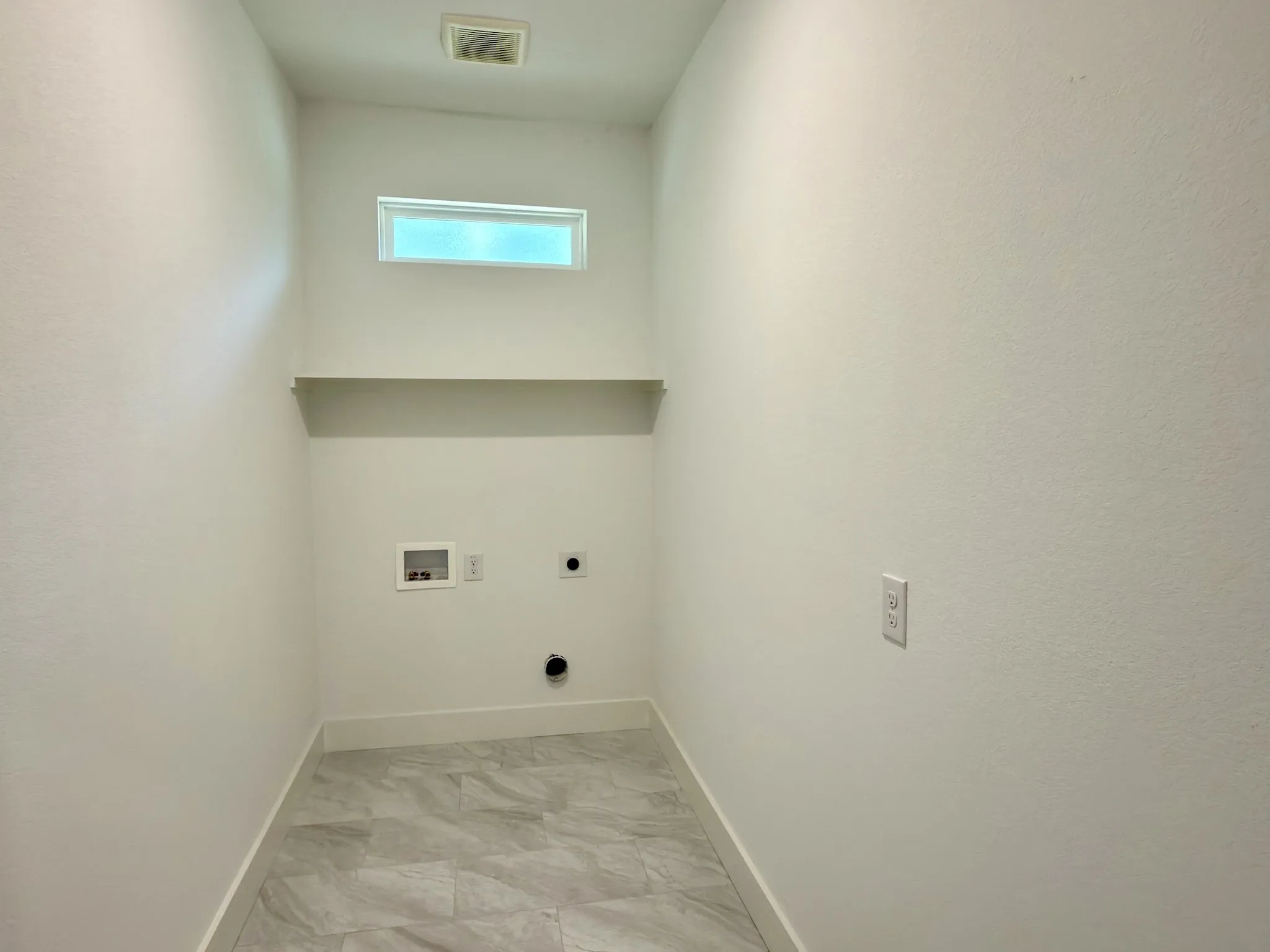 Dedicated utility space featuring tile flooring, a high transom window, and a built-in shelf