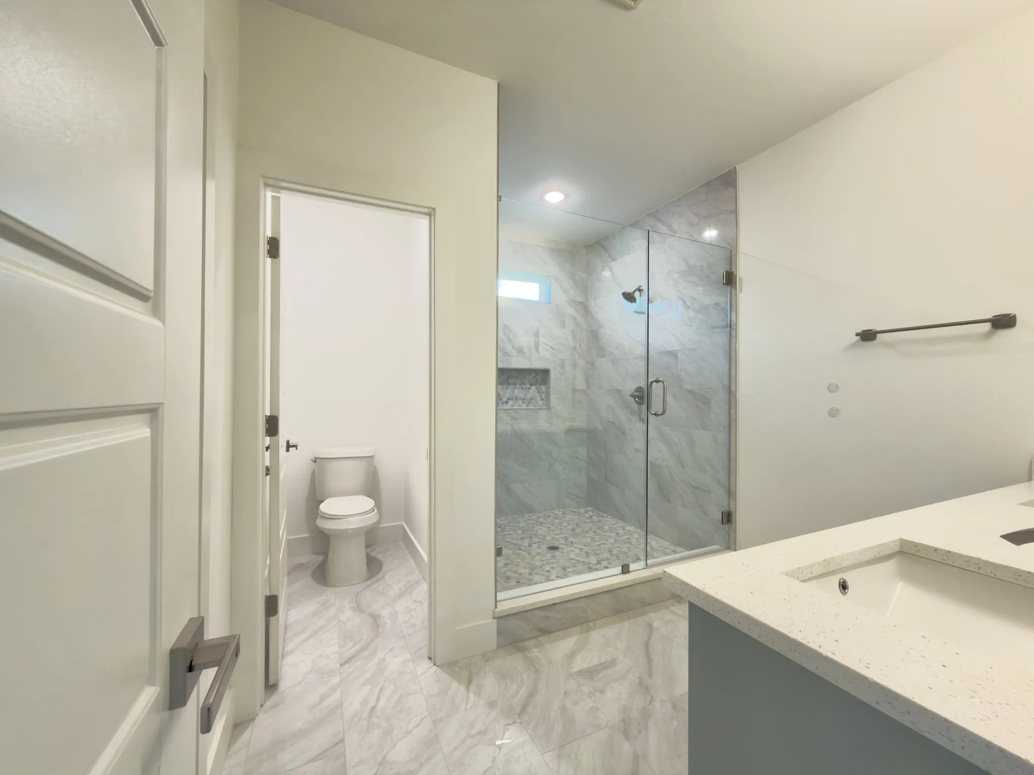 Contemporary bathroom featuring a glass-enclosed shower with pebble-tile floor, recessed lighting, and a window