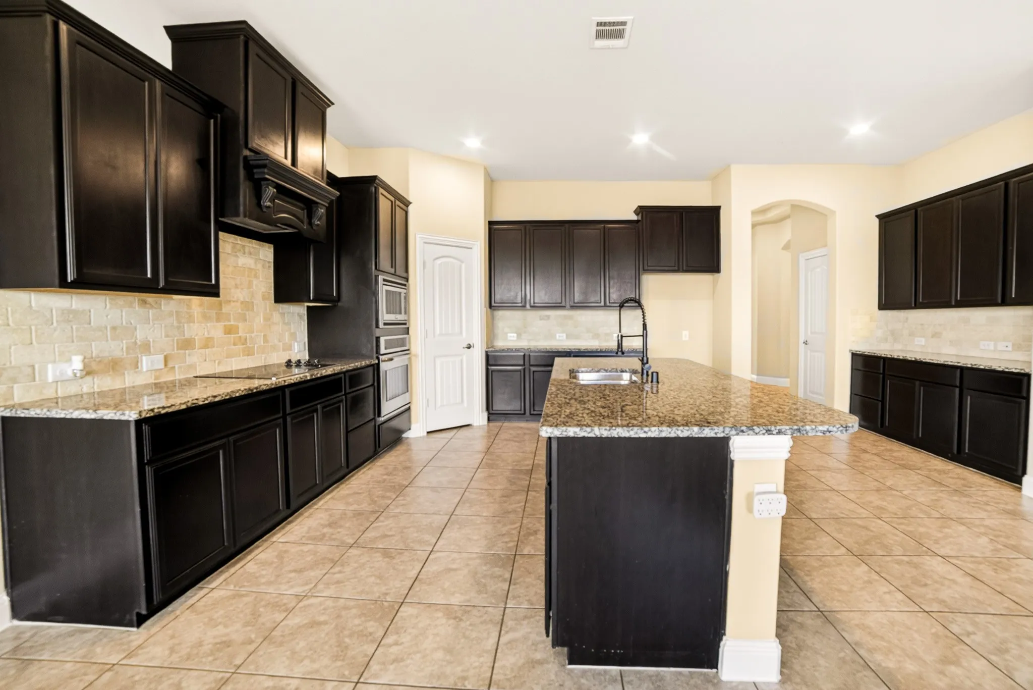 Full view of huge custom kitchen with recessed lights, custom upgraded 42inch shaker cabinets with granite counters and tiled back splashes. Builtin glass cooktop on left and then next to is built in oven & microwave, then walkin lighted pantry, then at far back extra cabinets with coffee bar and room for many counter appliances. On the right is the added butlers pantry cabinets and of course in the middle is the island with built in dishwasher, electric outlets at end of island, deep double sink, upgraded faucet, and the breakfast bar easily seats 4
