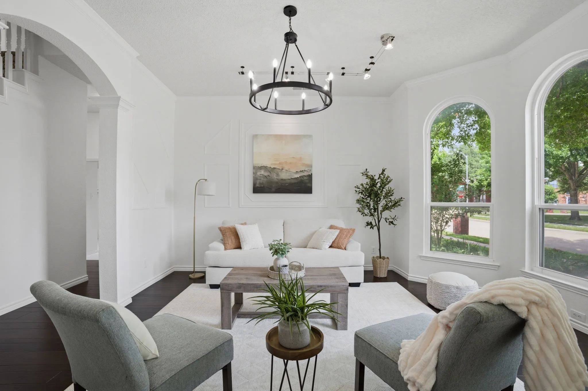 Bright living area featuring arch-top windows, dark wood-finish flooring, and a circular black iron chandelier