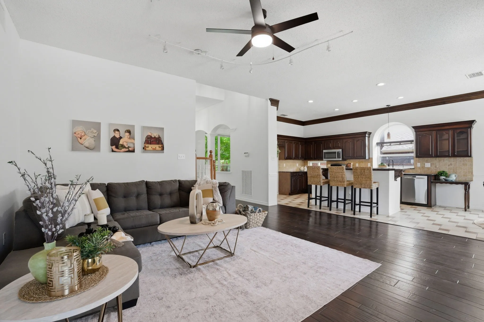 Open concept living area with dark wood-finish flooring extending into a kitchen featuring rich wood cabinetry, stainless steel appliances, and a breakfast bar with pendant lighting