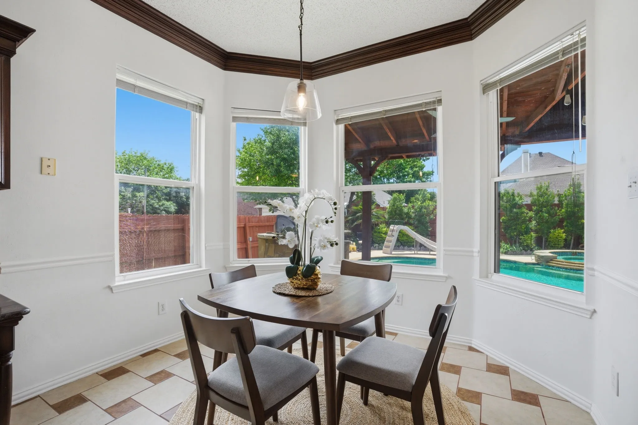 Breakfast nook with bay windows, patterned tile flooring, decorative crown molding, chair rail detailing, and a pendant light fixture
