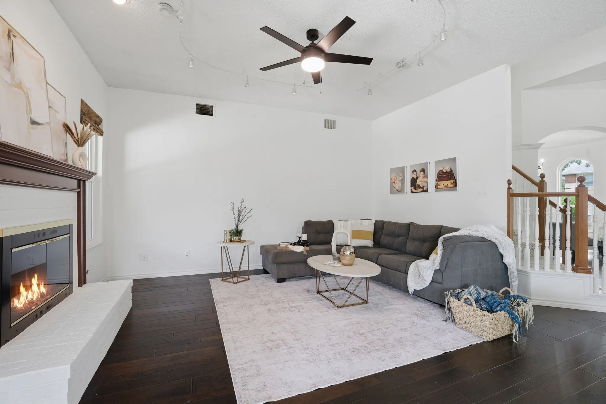 Living area featuring dark wood-finish flooring, a contemporary fireplace with a white hearth, and a ceiling fan with integrated lighting