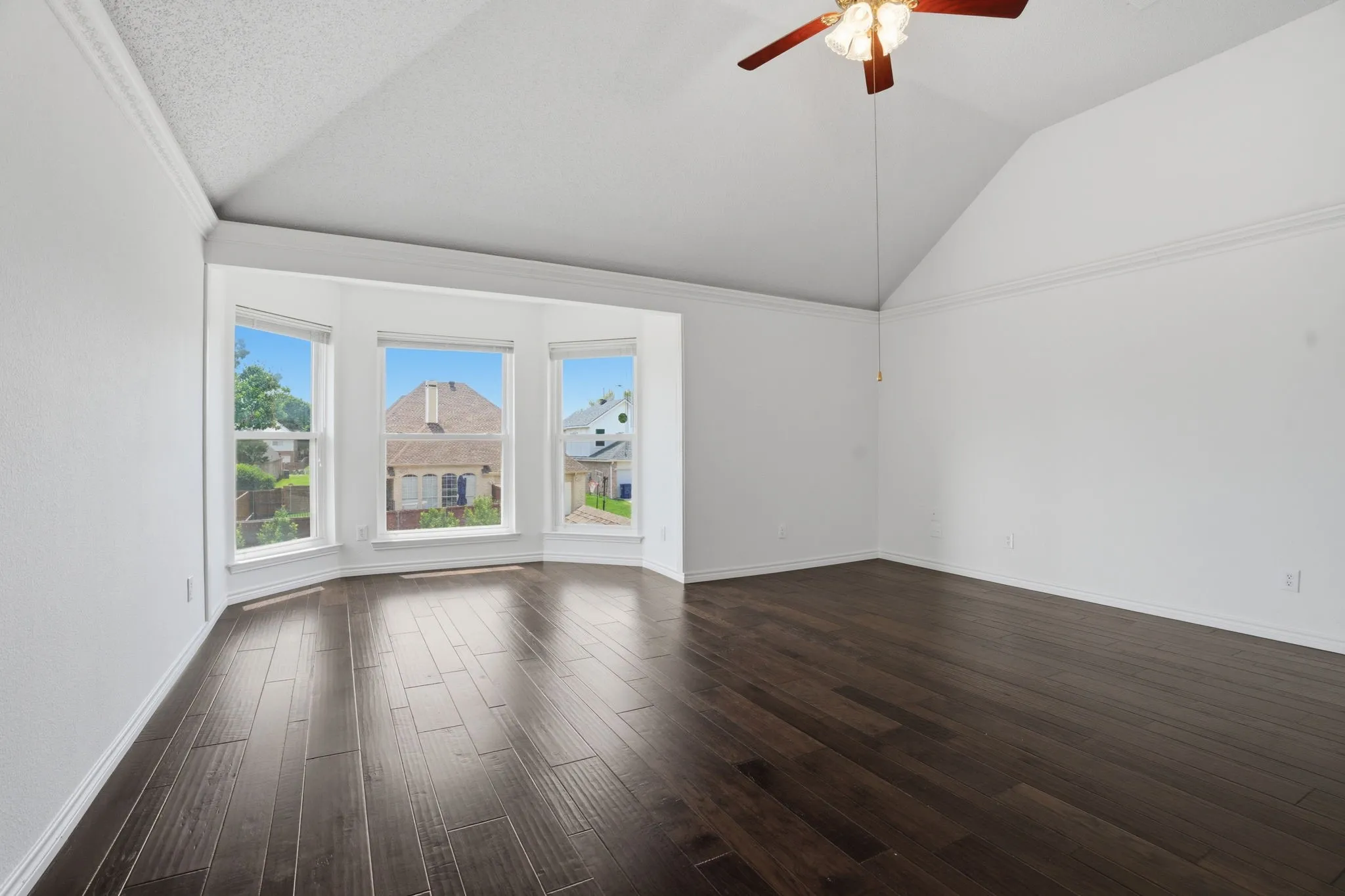 Spacious upstairs primary bedroom featuring vaulted ceilings, dark wood-finish flooring, a ceiling fan, and multiple windows with white trim