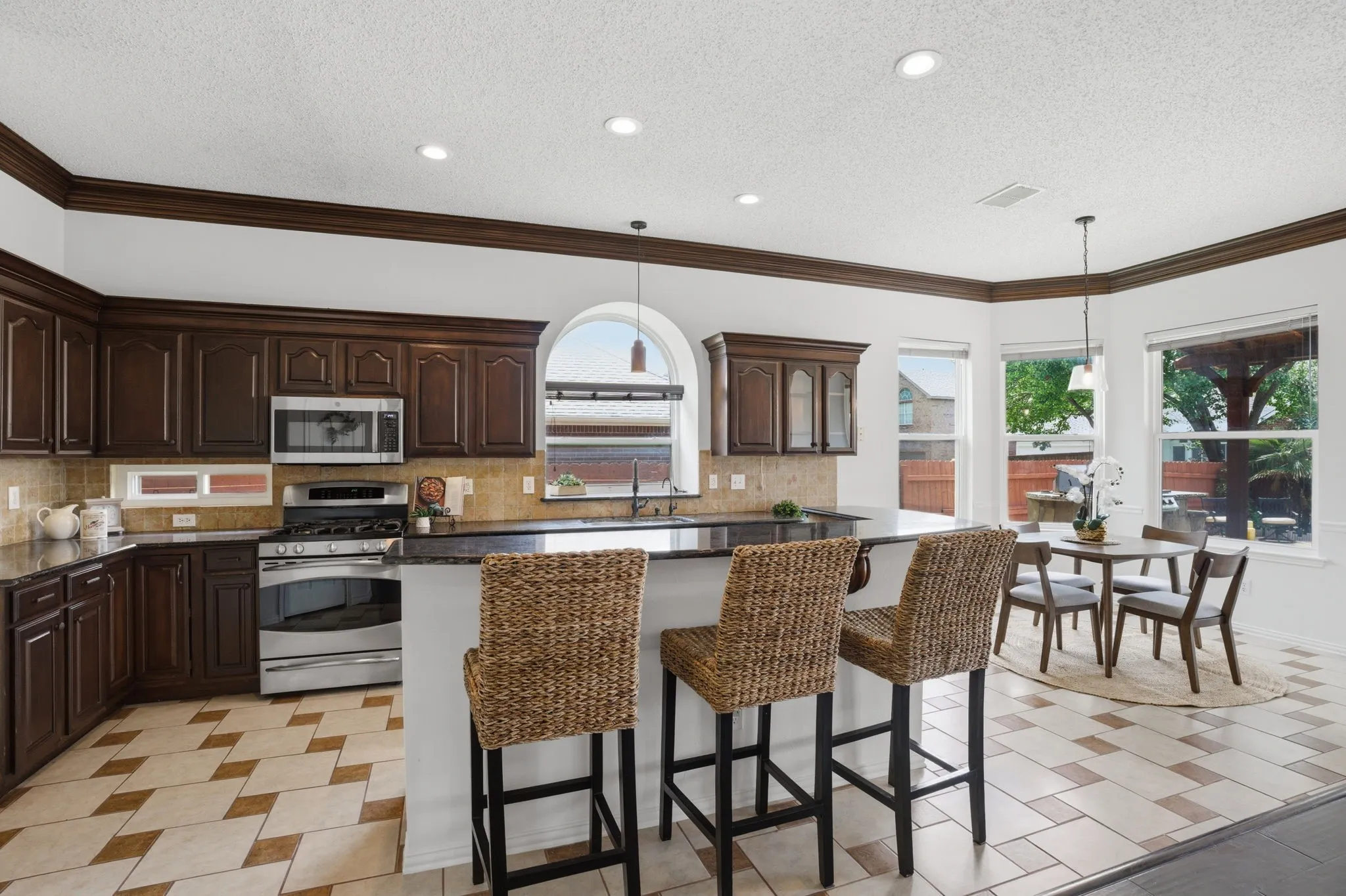 Open-concept kitchen featuring dark wood cabinetry, stainless steel appliances, granite countertops, and a tile backsplash