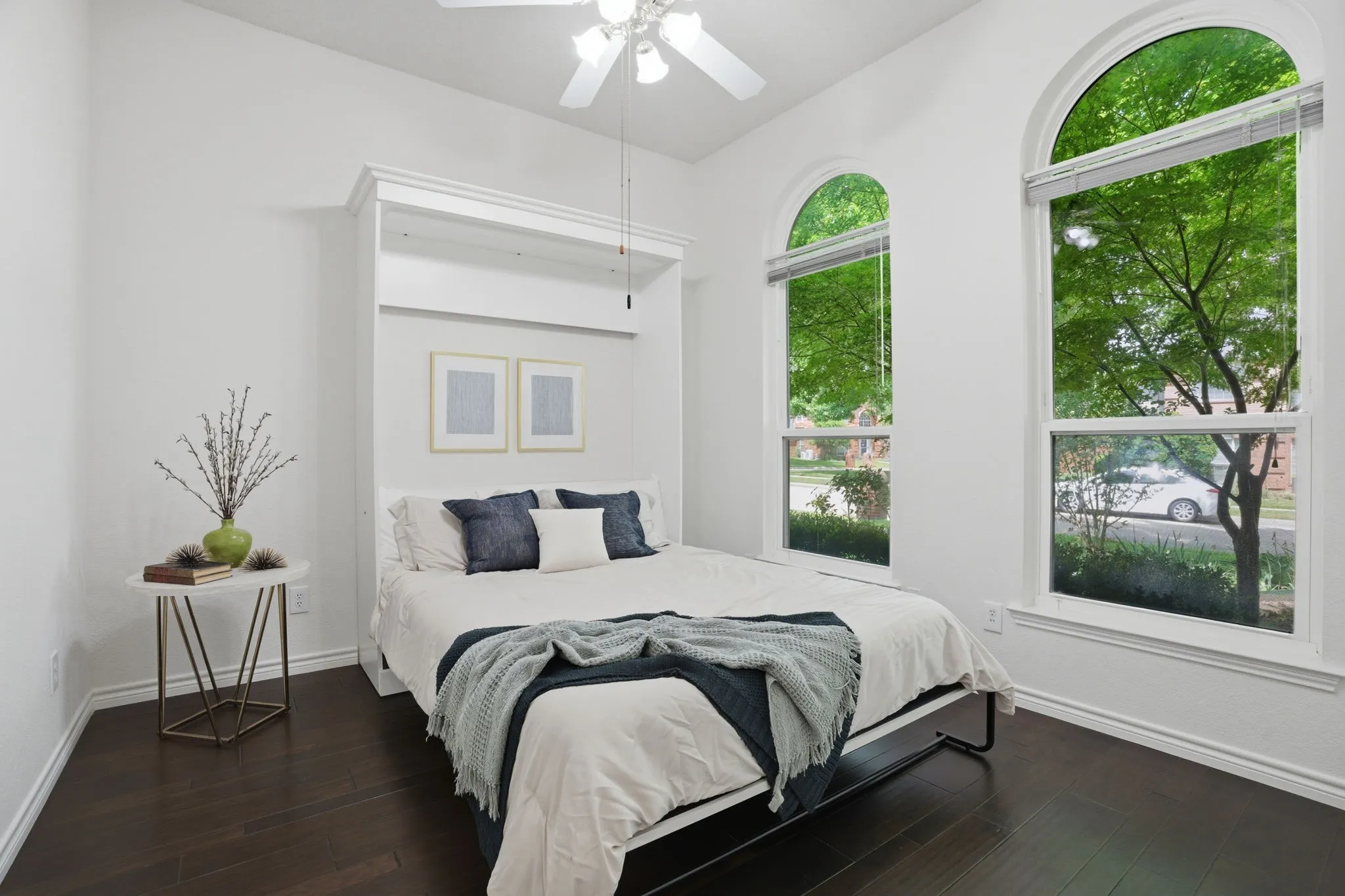 Downstairs secondary bedroom featuring dark wood-finish flooring, white walls, and a white ceiling fan