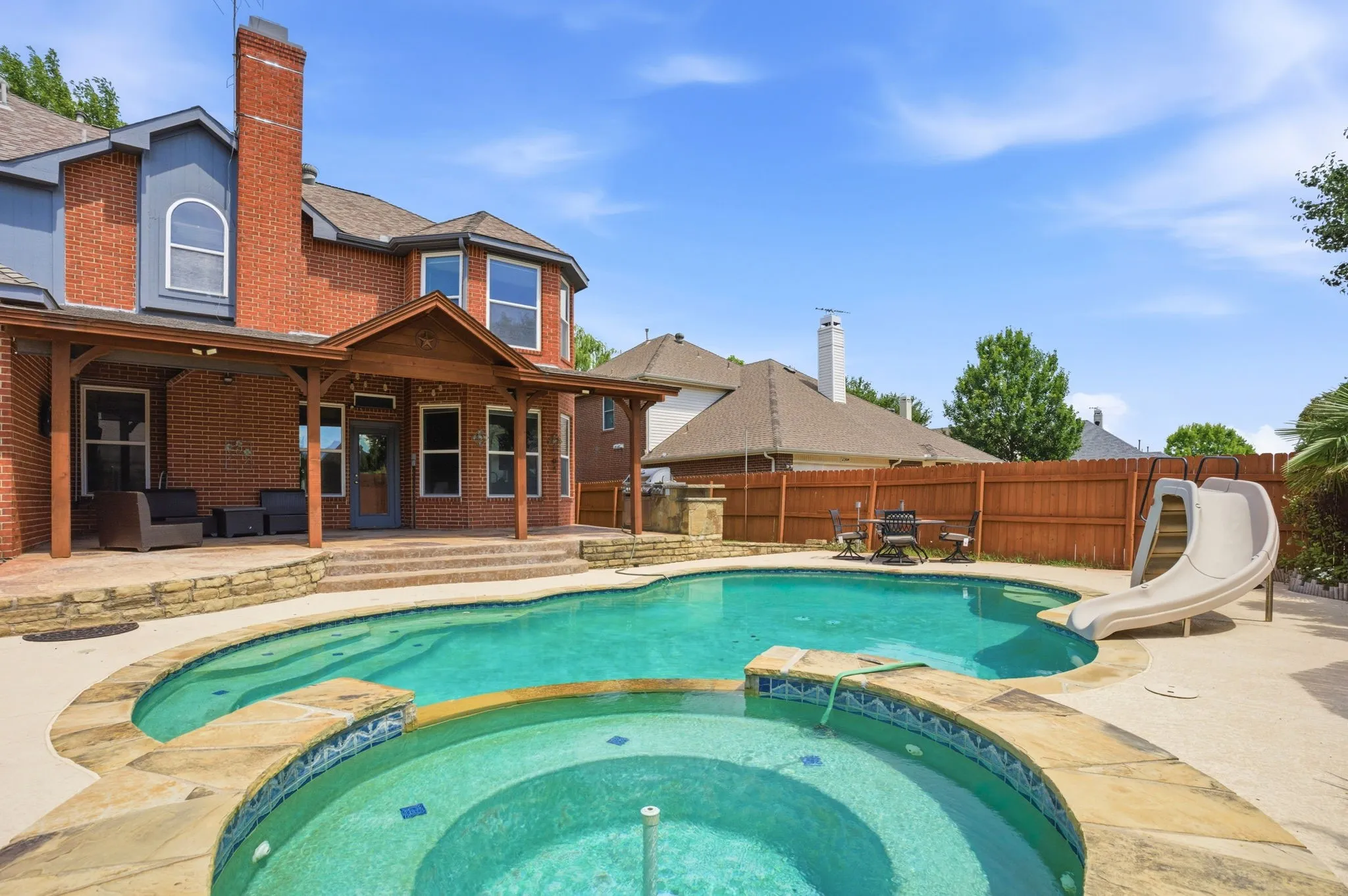Custom-shaped pool and spa with stone coping, featuring a built-in slide