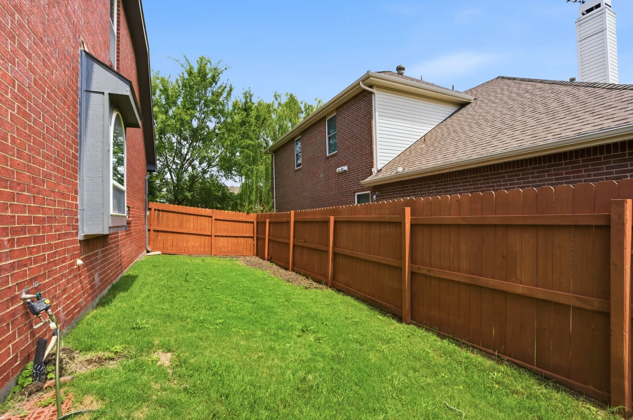 Enclosed backyard featuring a new wood privacy fence, a red brick exterior wall, a bay window with a gray frame, and a green lawn