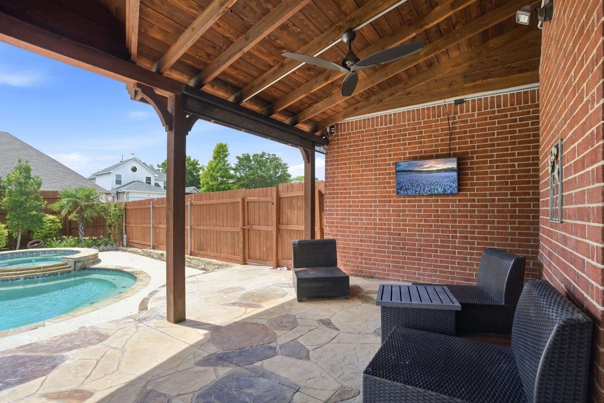 Expansive covered patio featuring a wood-finish ceiling with a ceiling fan, brick accent wall, stamped concrete flooring, and an outdoor television