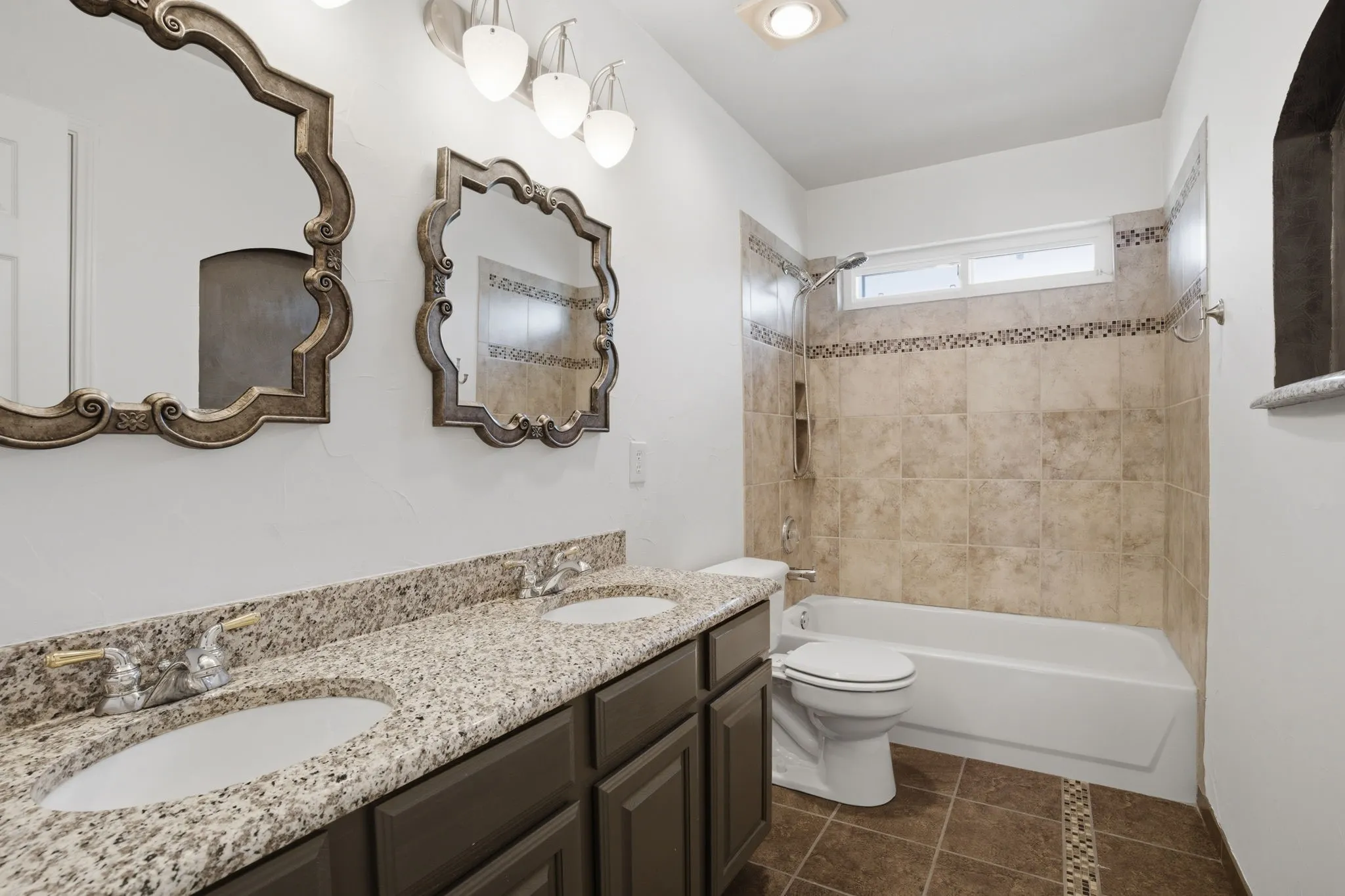 Bathroom featuring a dual vanity with granite-finish countertops and undermount sinks, a white tub, and a shower with tiled surround