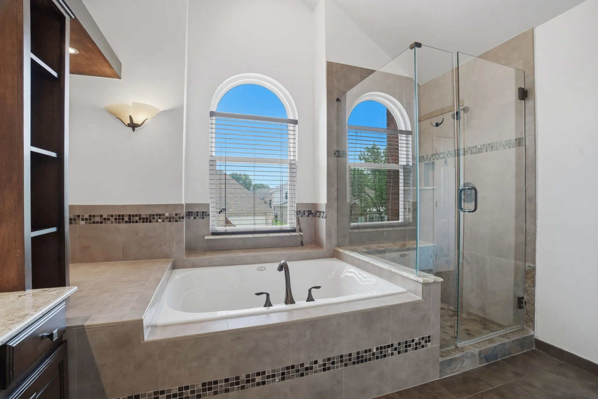 Soaking tub with bronze-finish fixtures, complemented by two arched windows with blinds