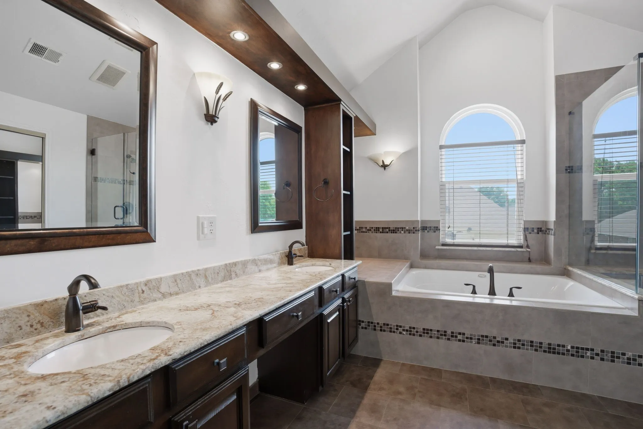 Bathroom featuring a built-in soaking tub, arched windows, dual vanity with undermount sinks, and dark wood-finish cabinetry