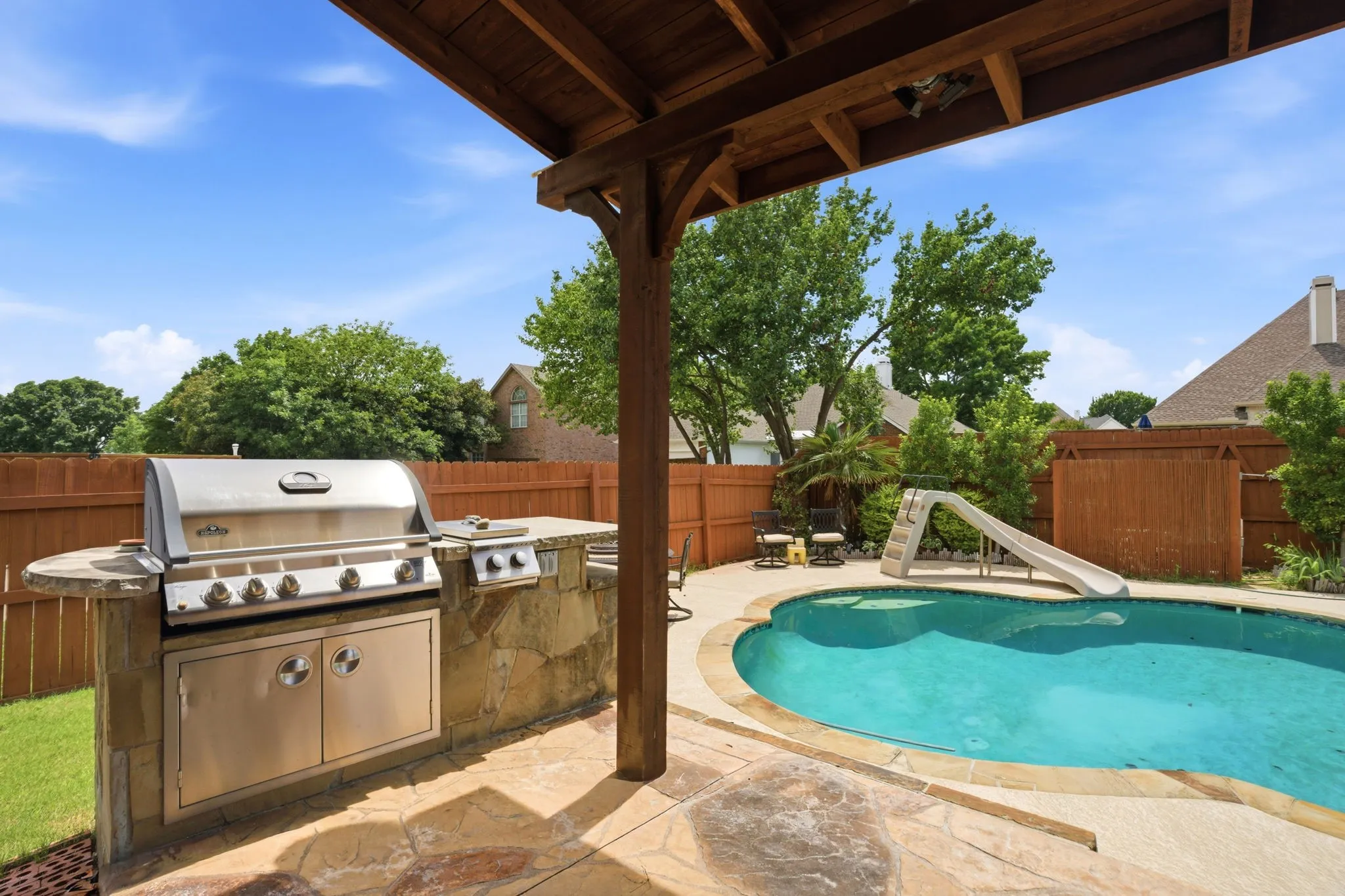 Covered patio featuring an outdoor kitchen with built-in grill and stone base, a freeform swimming pool, and stone-finish patio flooring