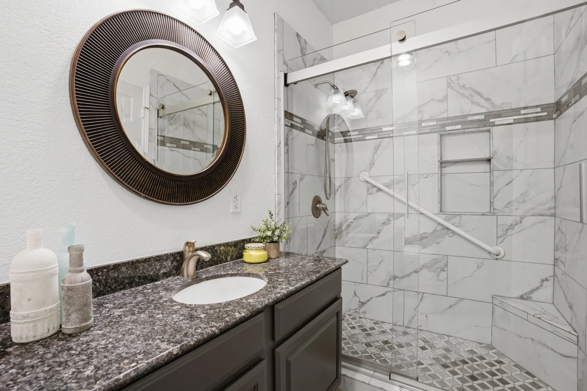 Downstairs secondary  bathroom featuring a dark vanity with a speckled countertop, an undermount sink, and a bronze-framed round mirror