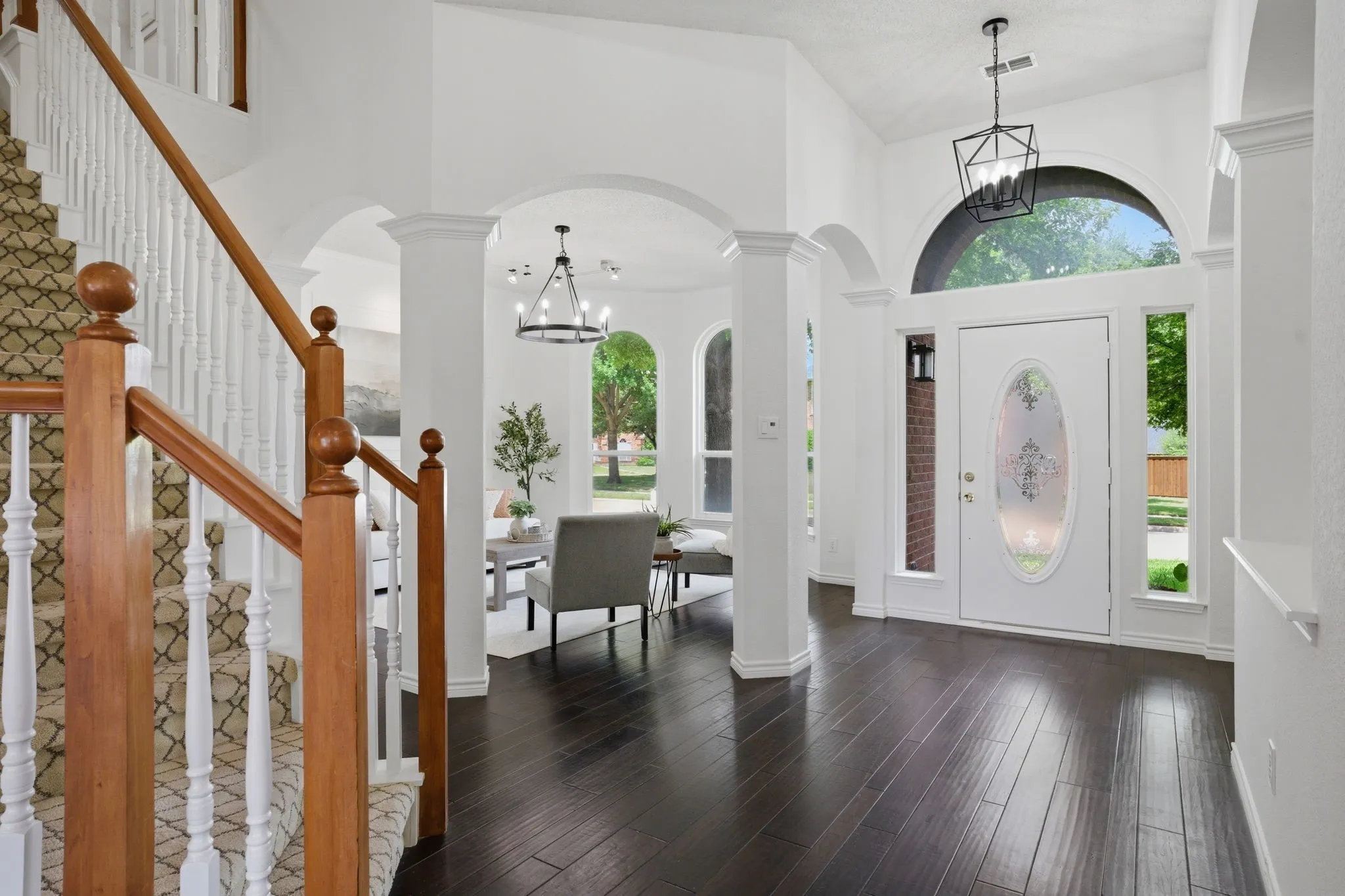 Two-story foyer featuring dark wood-finish flooring, a grand staircase with white balusters and wooden banister, and a decorative frosted glass front door