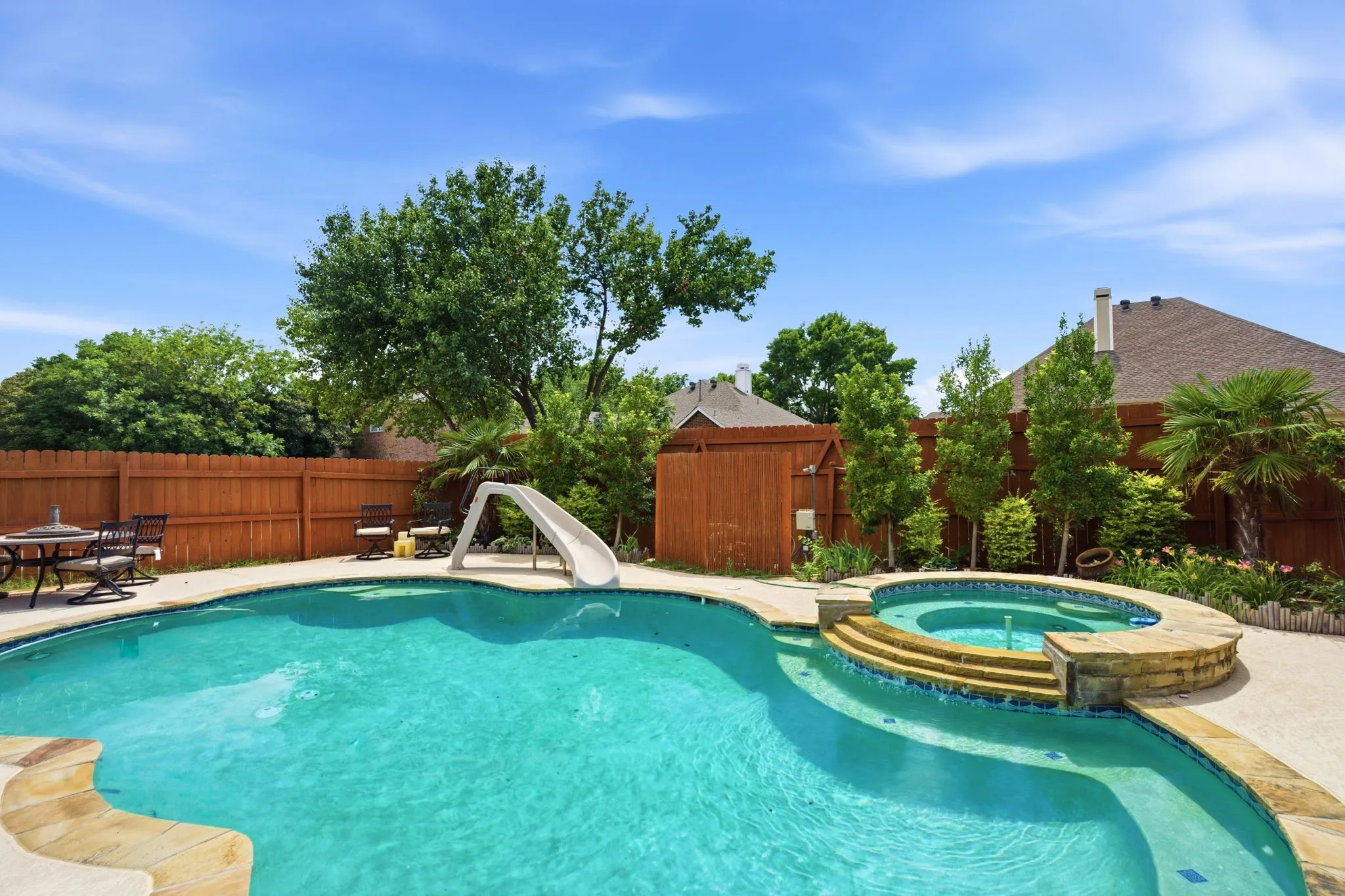 Inviting backyard featuring a freeform swimming pool with integrated spa and waterfall, surrounded by concrete decking and a wood privacy fence