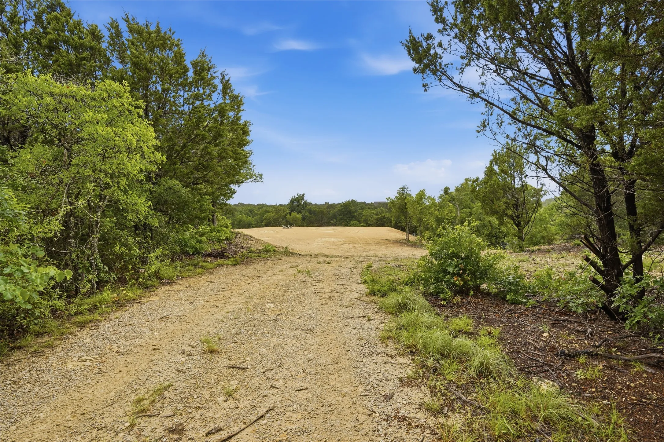 Gravel driveway leading to your homesite framed by dense mature trees and lush green foliage