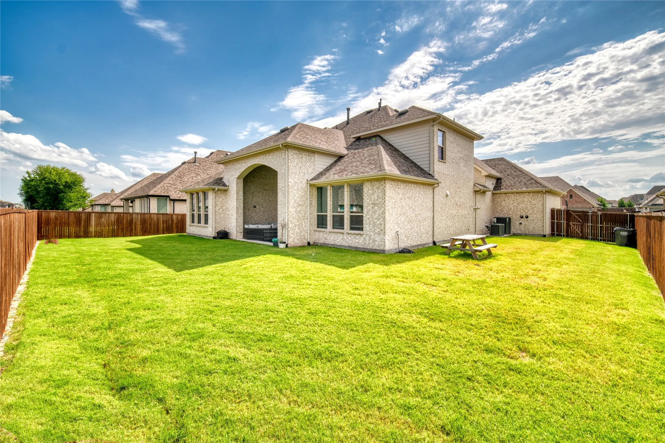 Rear view of property with a fenced backyard, brick siding, and roof with shingles