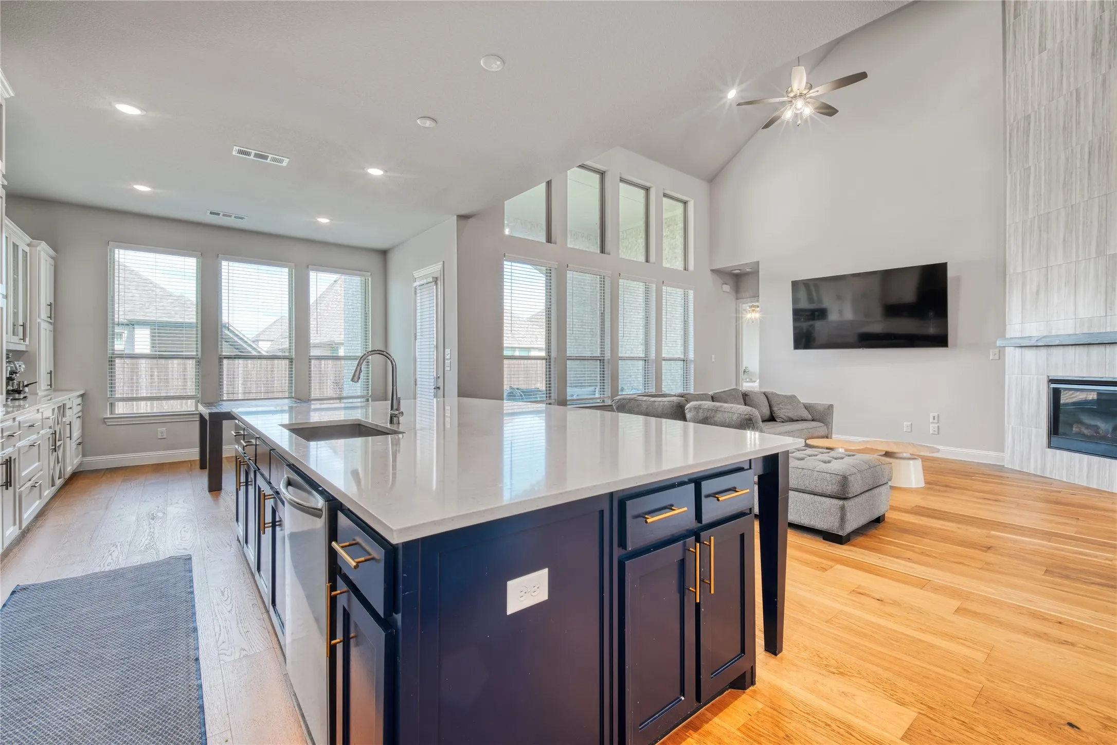 Kitchen with light wood-type flooring, blue cabinetry, an island with sink, a tiled fireplace, and open floor plan