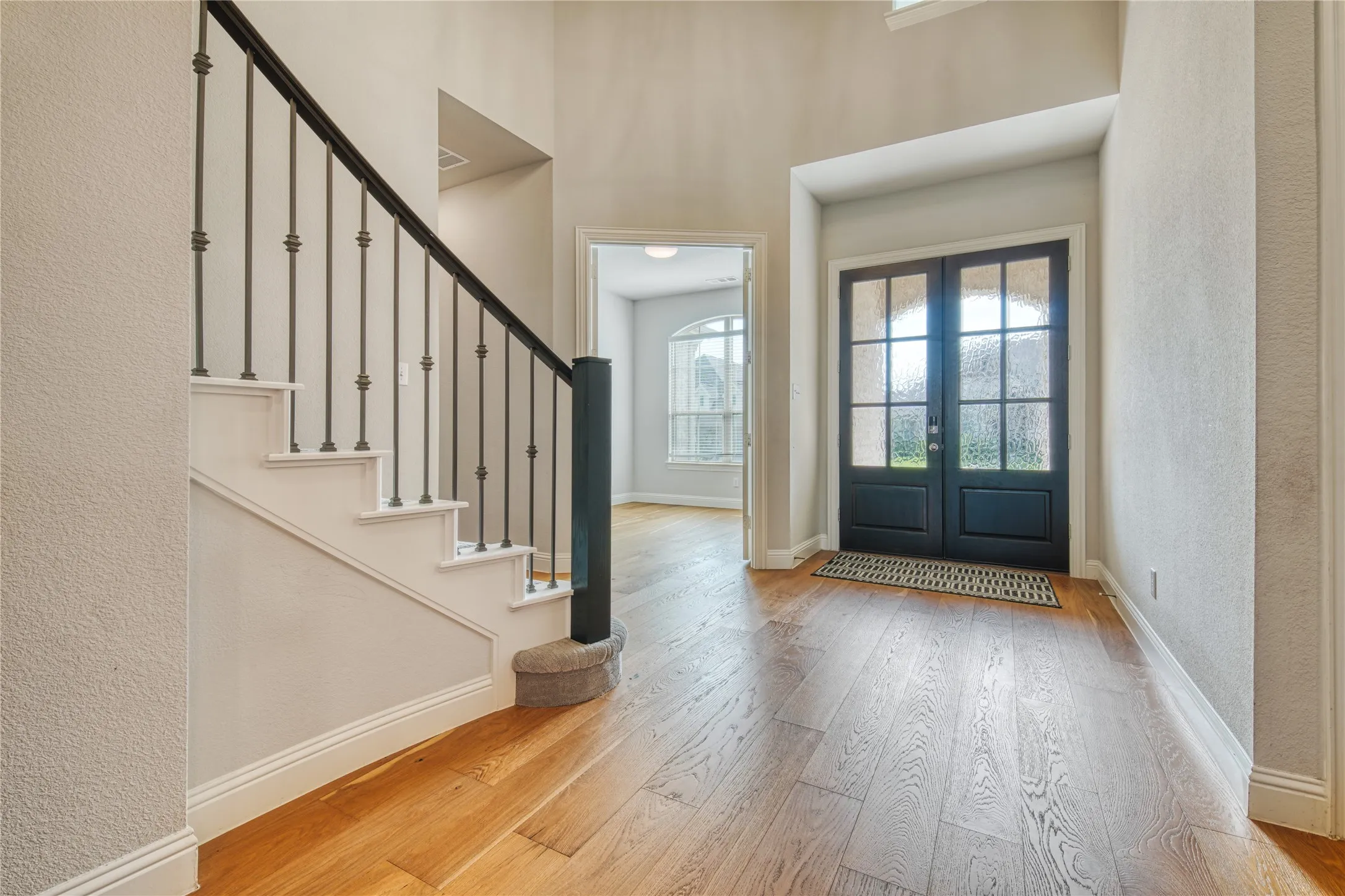 Foyer featuring hardwood / wood-style floors, stairway, a textured wall, a towering ceiling, and french doors