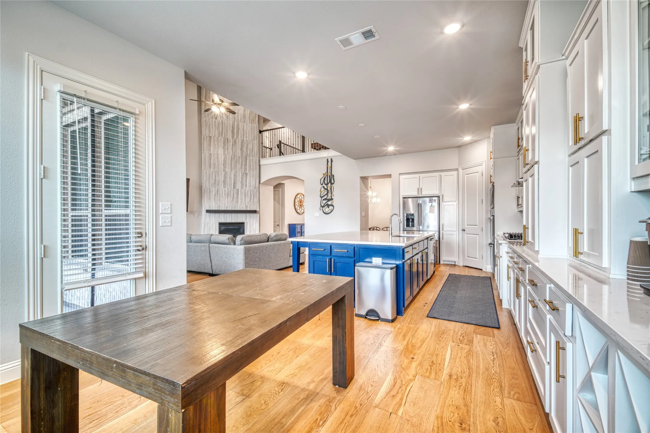 Kitchen featuring blue cabinets, an island with sink, light wood-style flooring, arched walkways, and white cabinets
