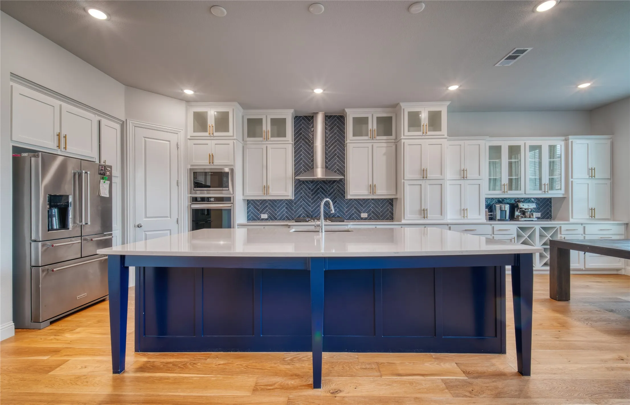Kitchen featuring appliances with stainless steel finishes, white cabinetry, light countertops, an island with sink, and recessed lighting