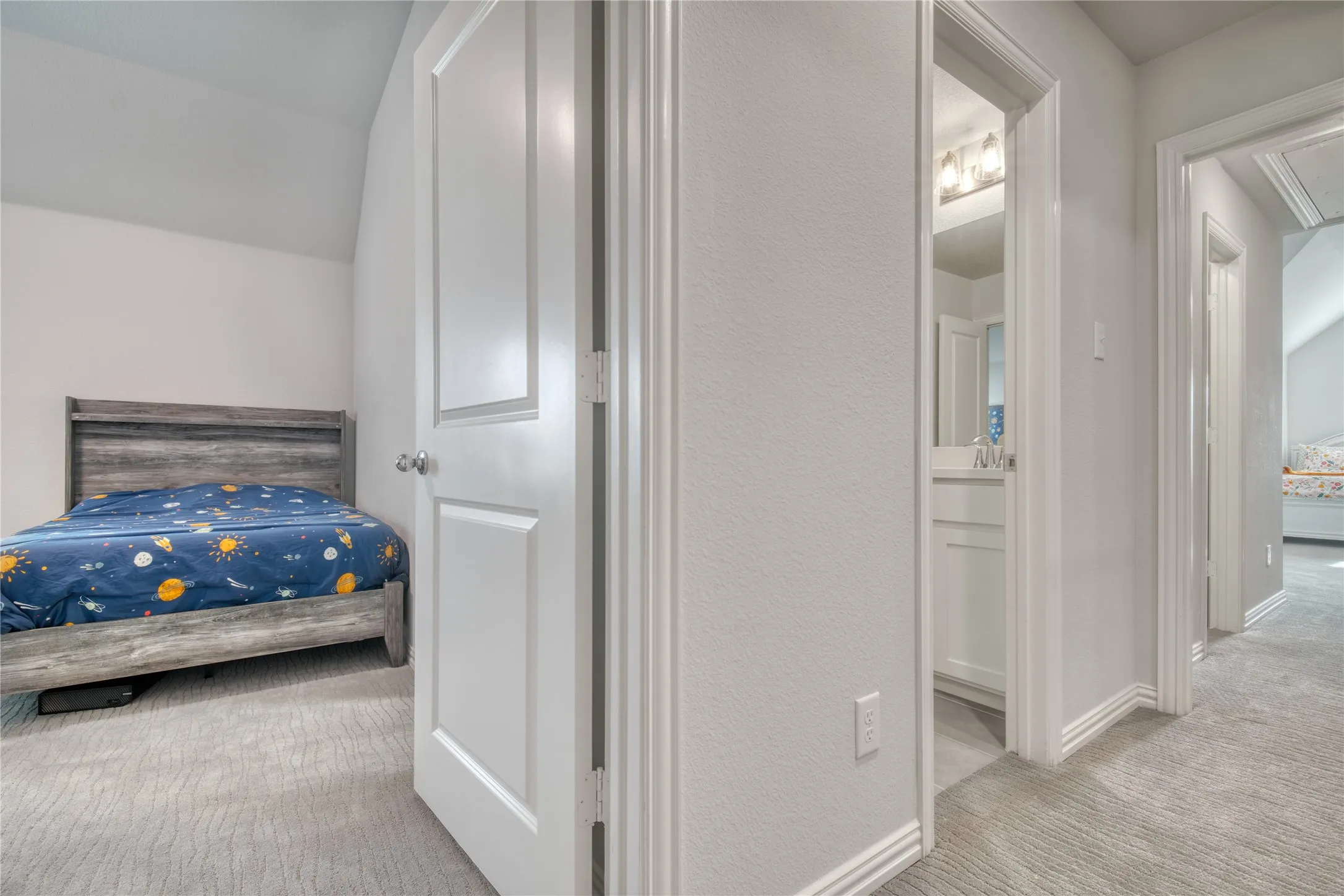 Carpeted bedroom featuring ensuite bathroom, lofted ceiling, and a textured wall